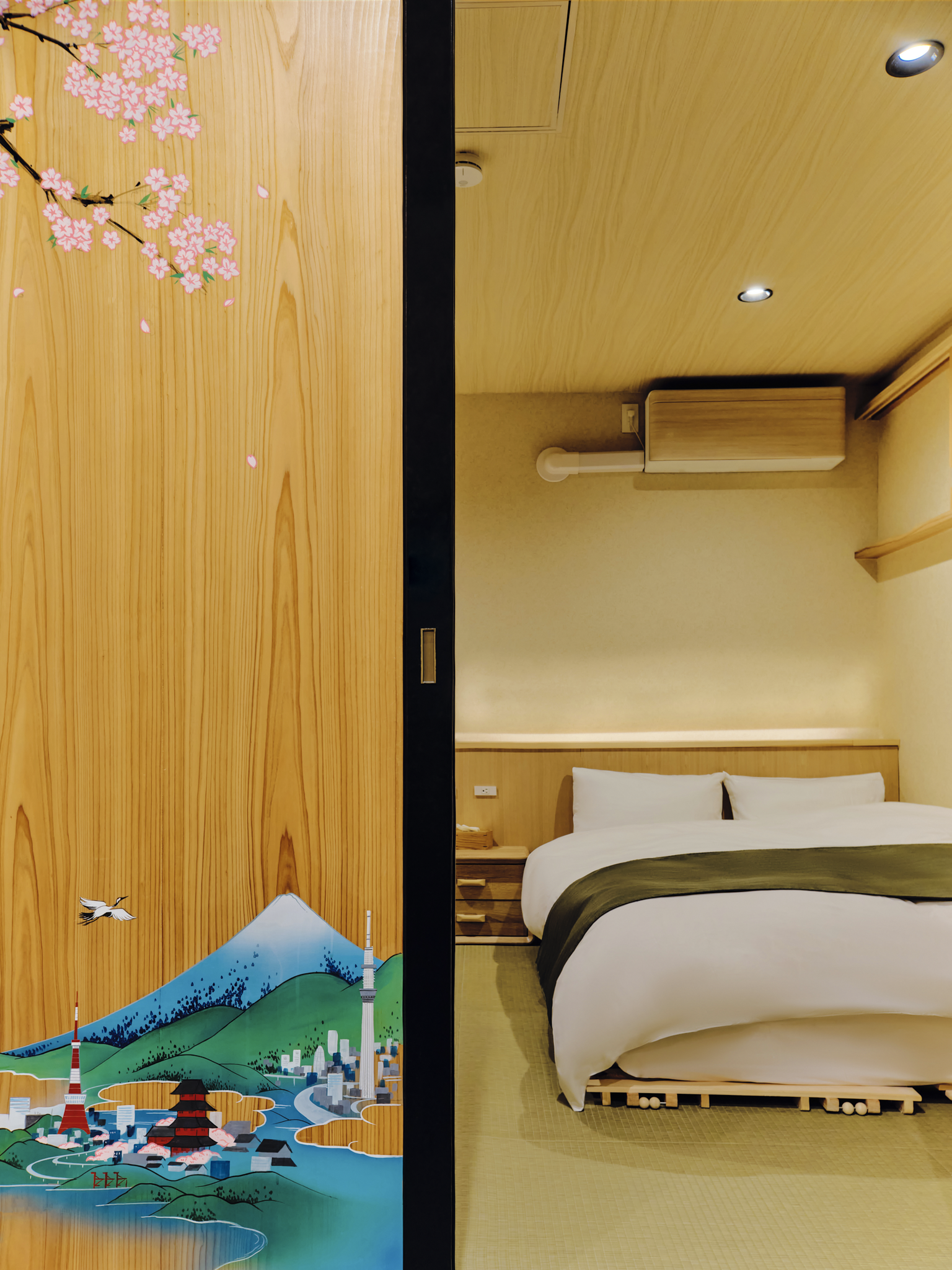 Room divider with traditional Japanese artwork of cherry blossoms and Mount Fuji, separating a decorated door from a bedroom with a bed and wooden furniture.