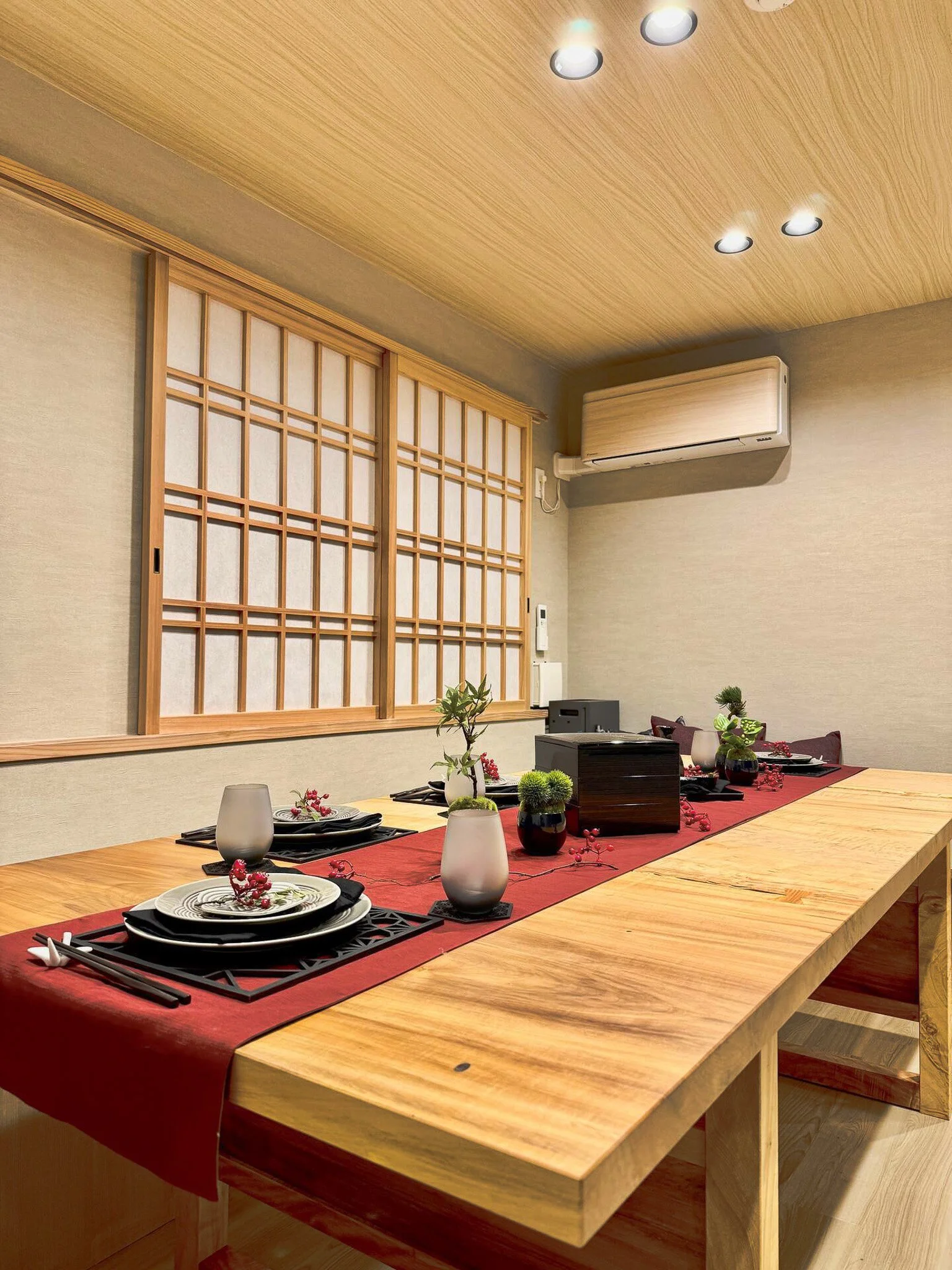 A traditional Japanese-style dining room with a wooden table, decorative table setting, shoji-style window, and air conditioning unit.