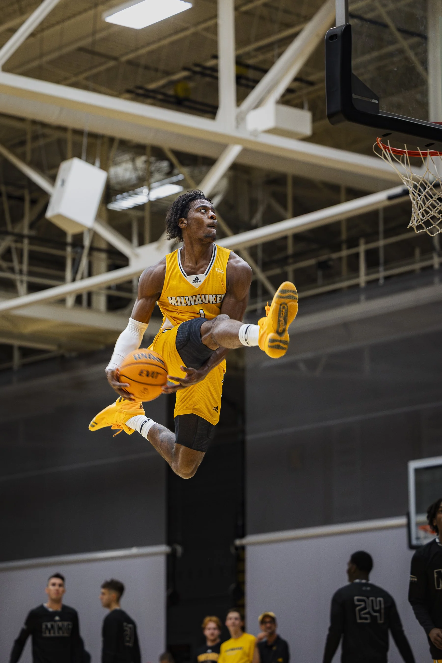 A basketball player in a yellow Milwaukee jersey mid-air, performing a dunk or layup during a game or practice in an indoor basketball court.