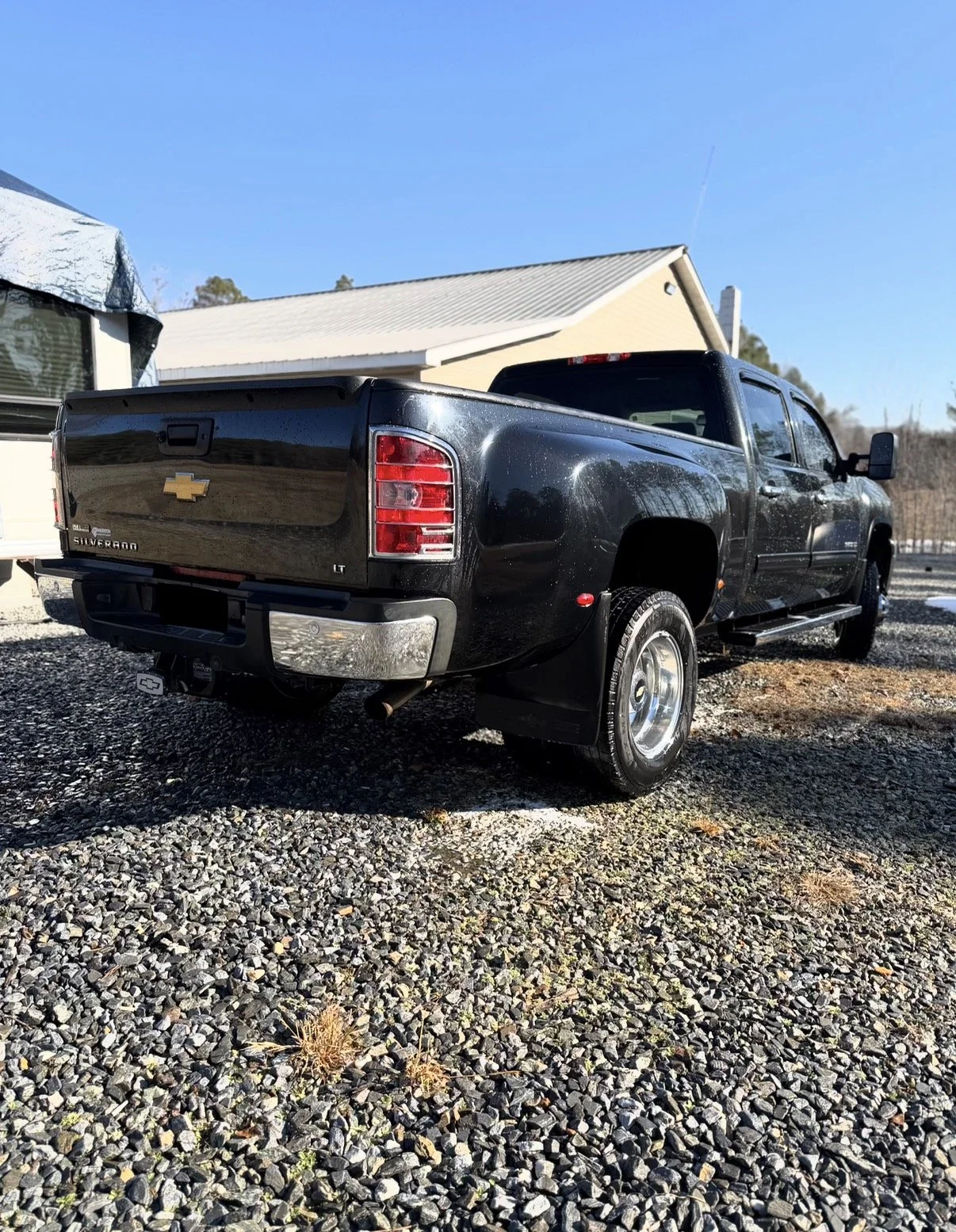 Black Chevrolet Silverado LT pickup truck parked on gravel driveway with a house and blue sky in the background.