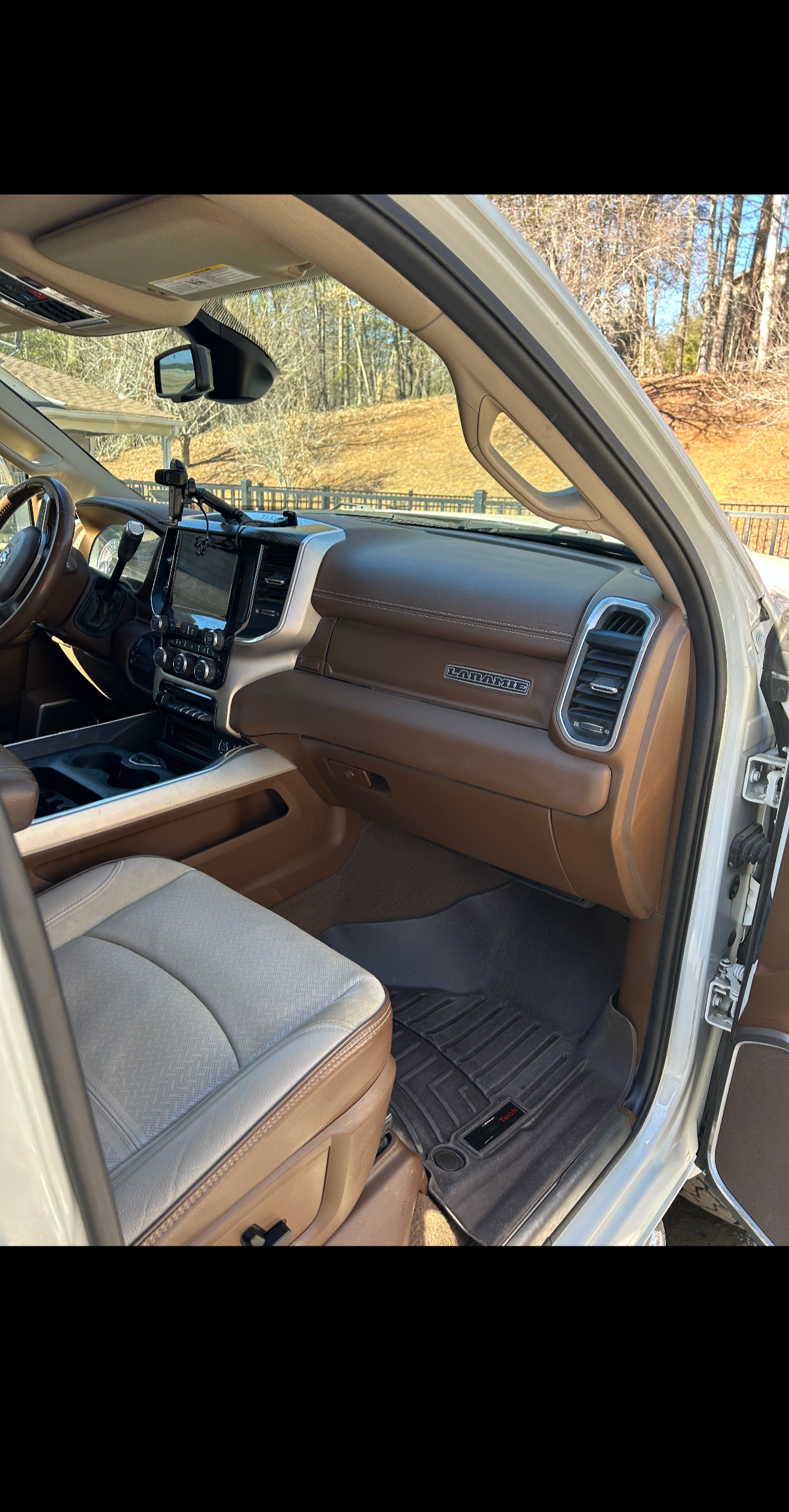 Interior of a tan and brown pickup truck with a dashboard, steering wheel, center console, and front seat. The scene is outdoors with trees and a fence in the background.