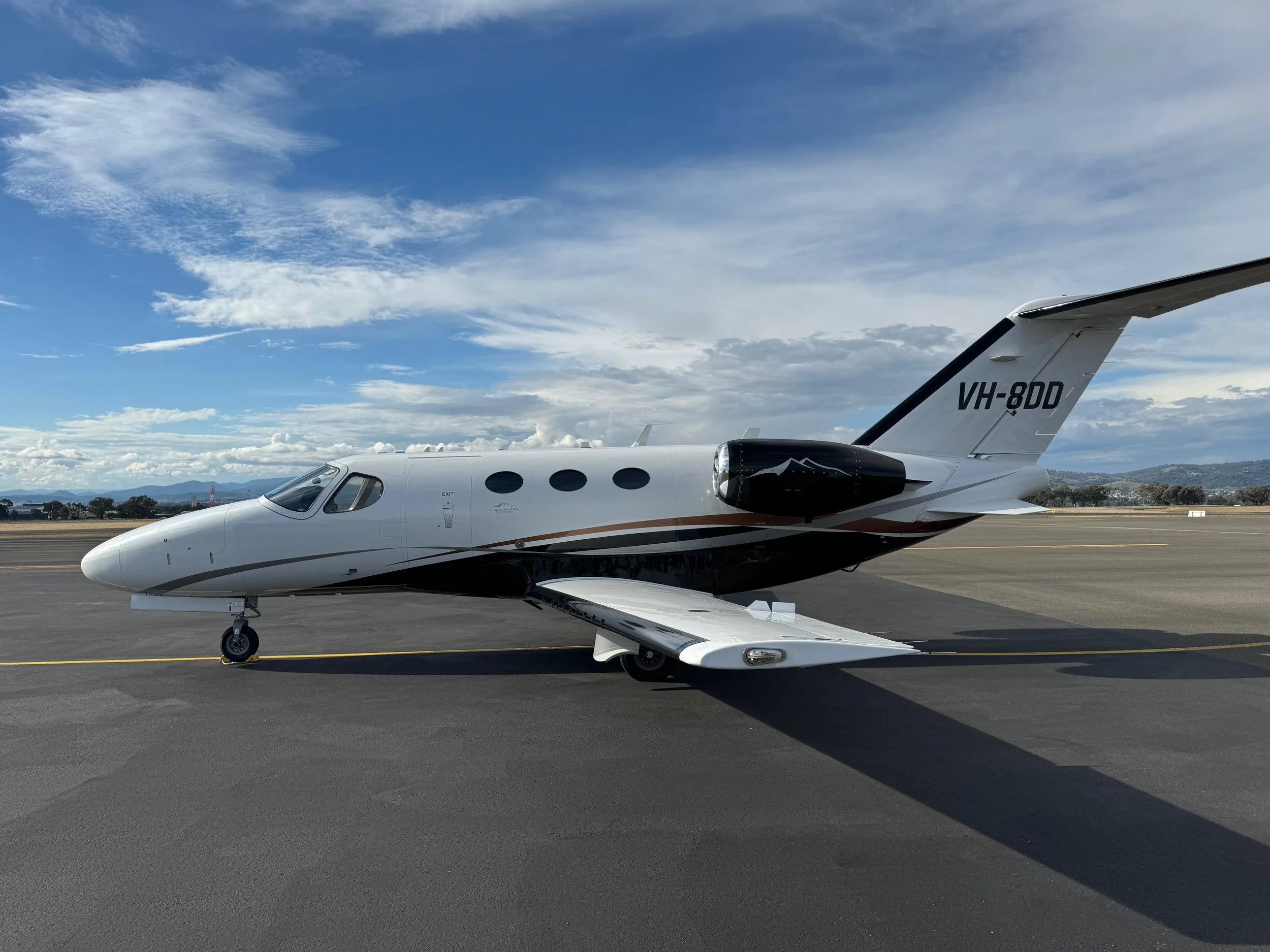 A white private jet with black and gold accents parked on an airport tarmac under a partly cloudy sky.