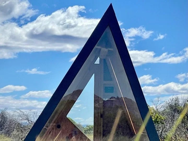 Close-up view of a triangular reflective monument with mountains and blue sky reflected on its surface.