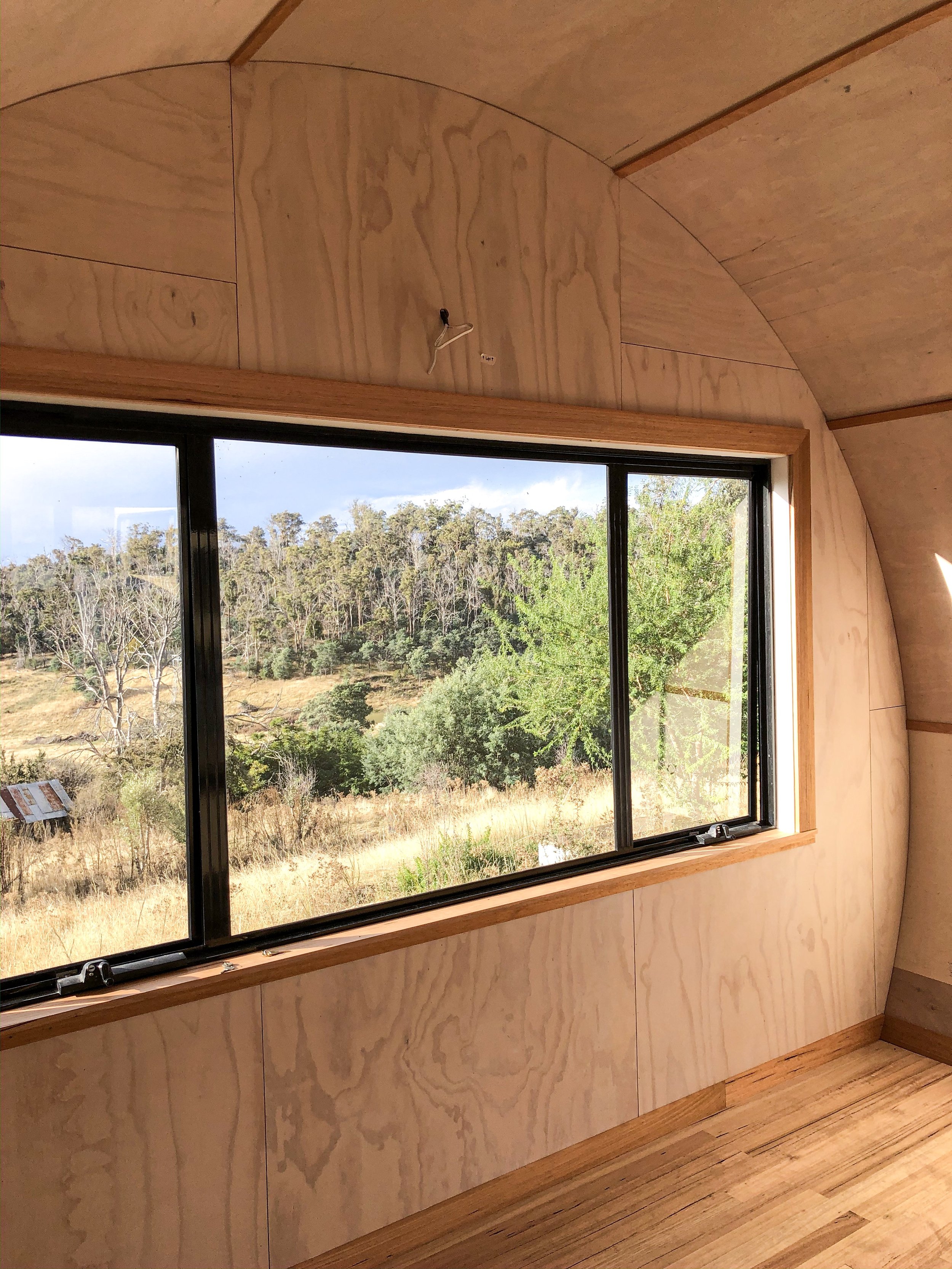 Interior of a wooden room with a large window showing a landscape of trees and grass outside.