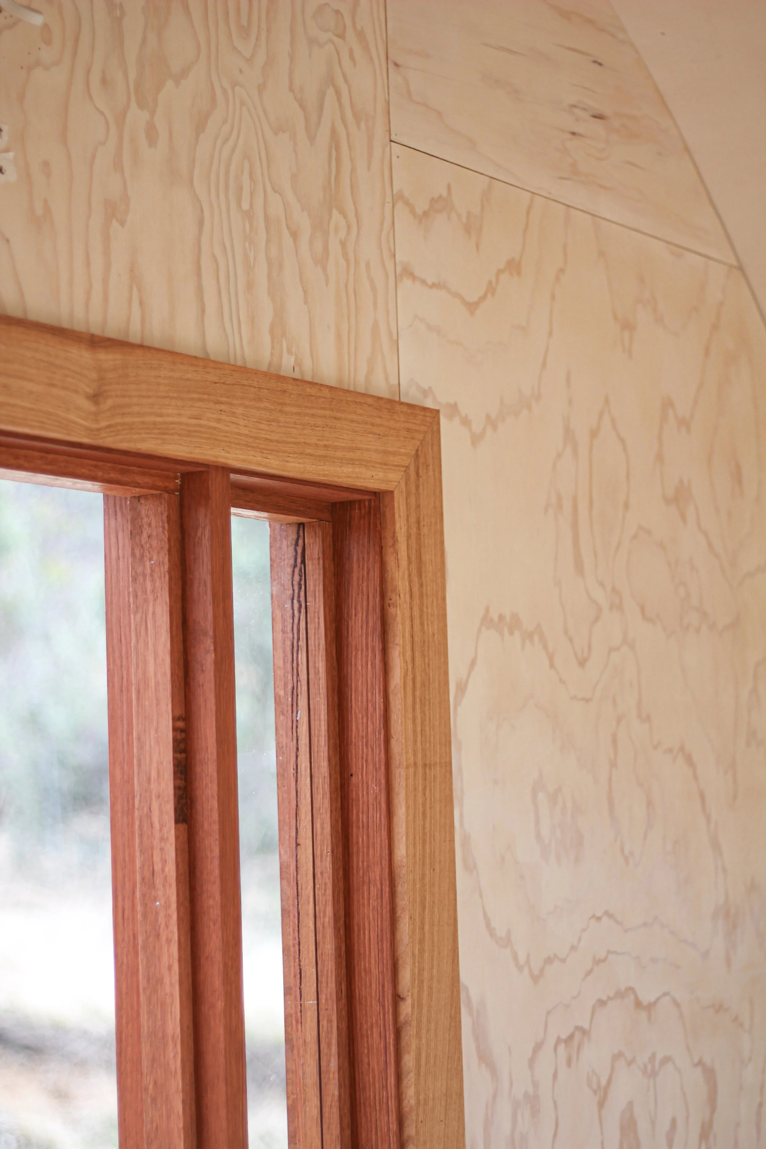 Close-up of interior corner of a wood-frame window with plywood panel walls.