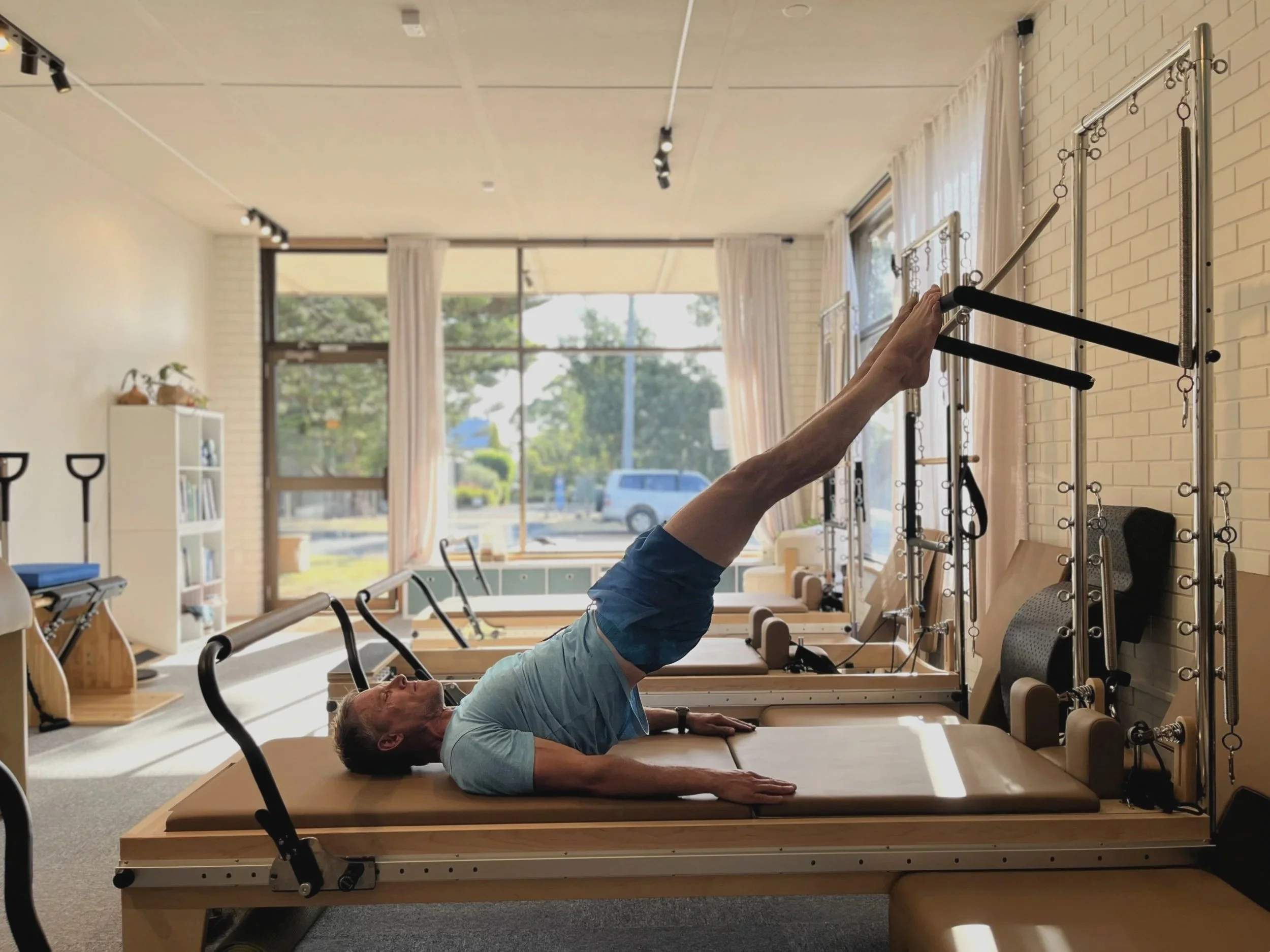 Athlete on Pilates reformer tower contemporary Pilates studio with large windows and natural light.