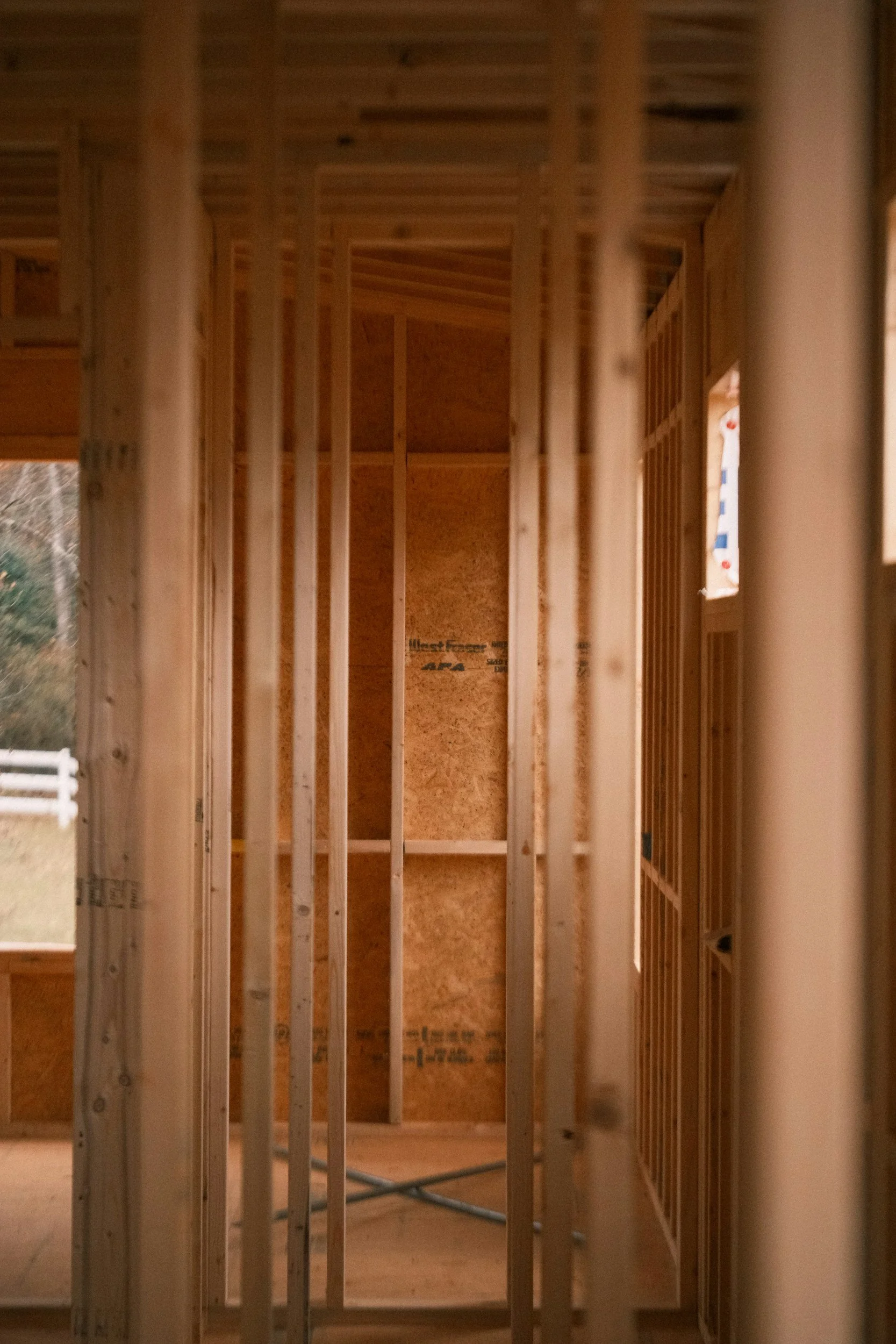 Interior view of a house under construction showing wooden framing and wall sheathing.