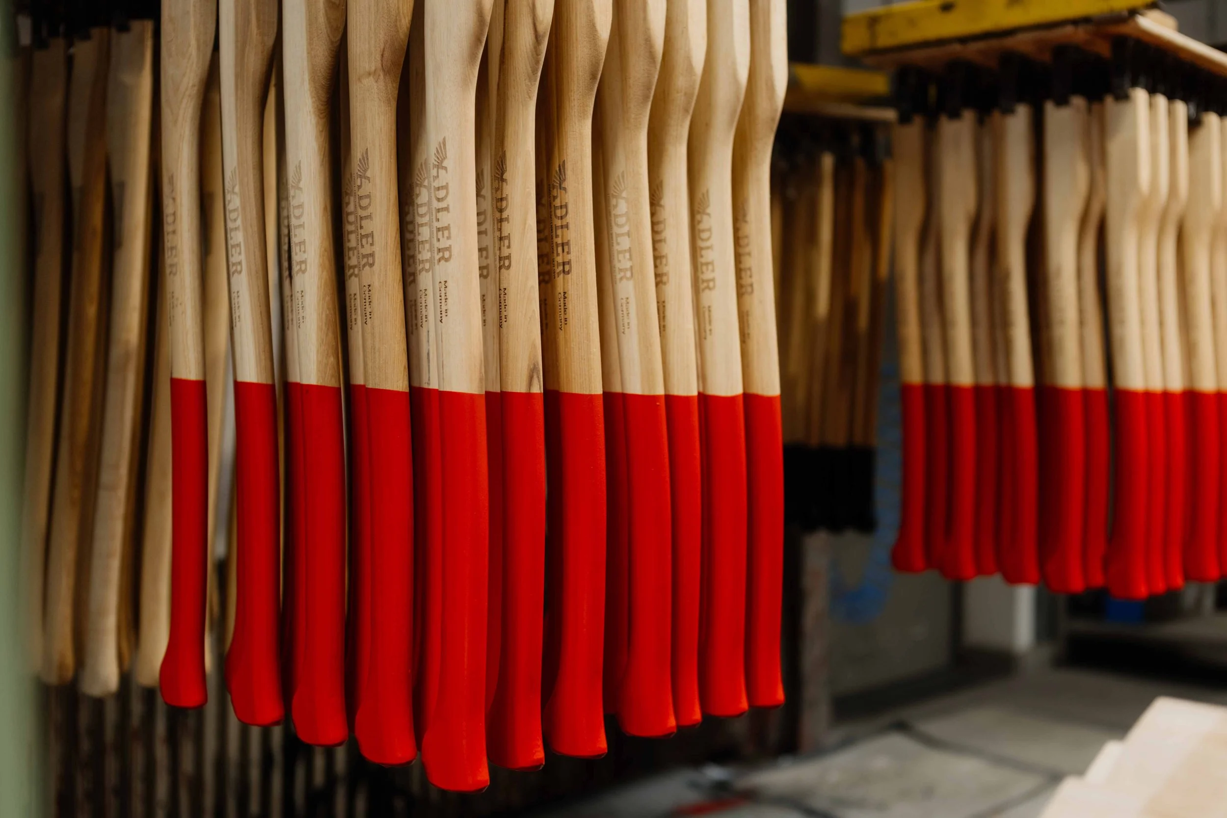 A row of wooden shovels with red blades hanging on a wall.