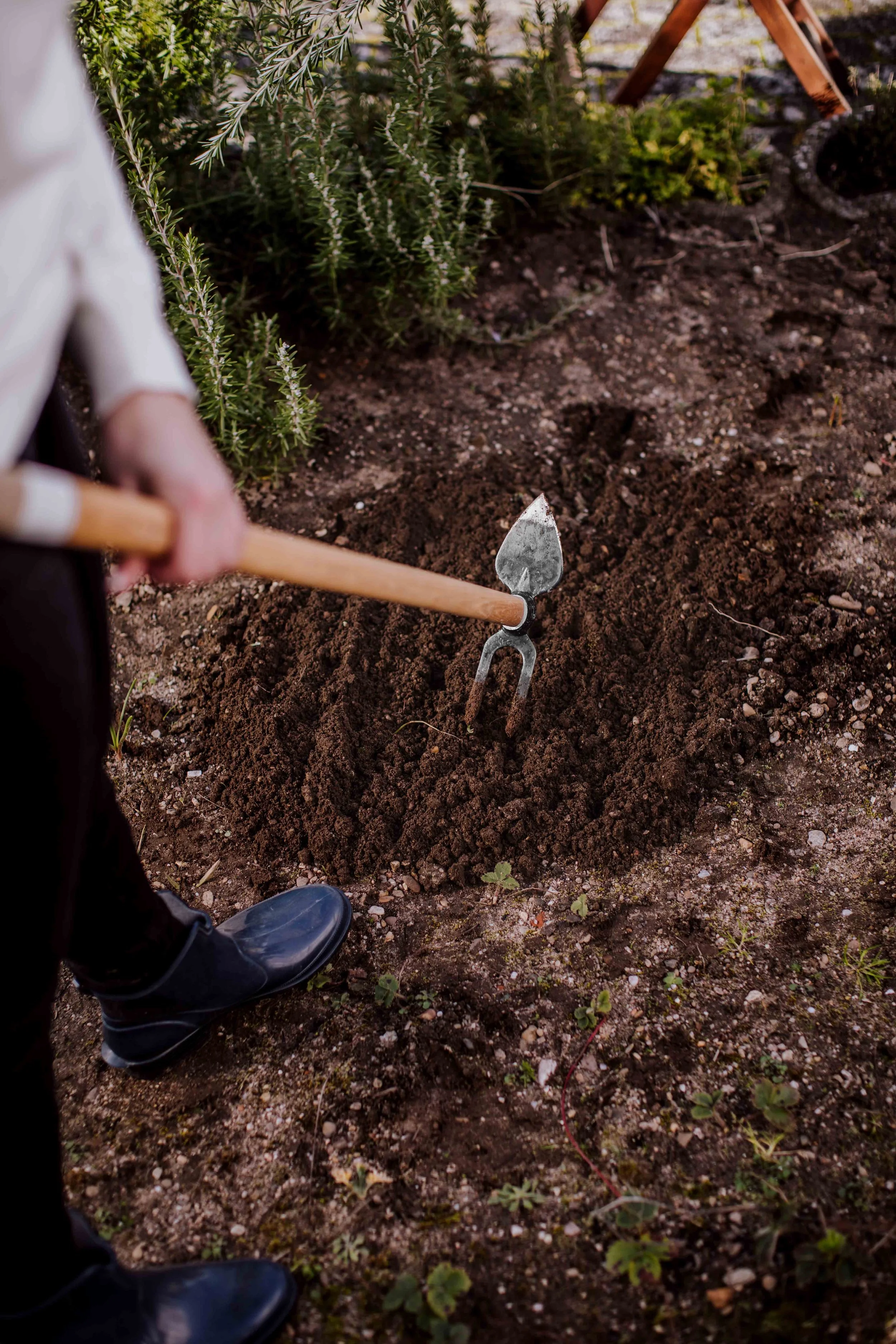 Person using gardening tools to dig a hole in the soil for planting in a garden.