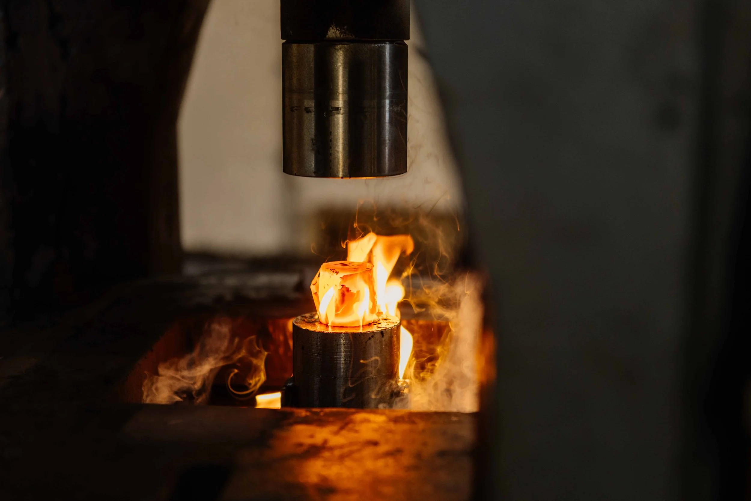 Close-up of hot metal being forged under a press, with sparks and flames.