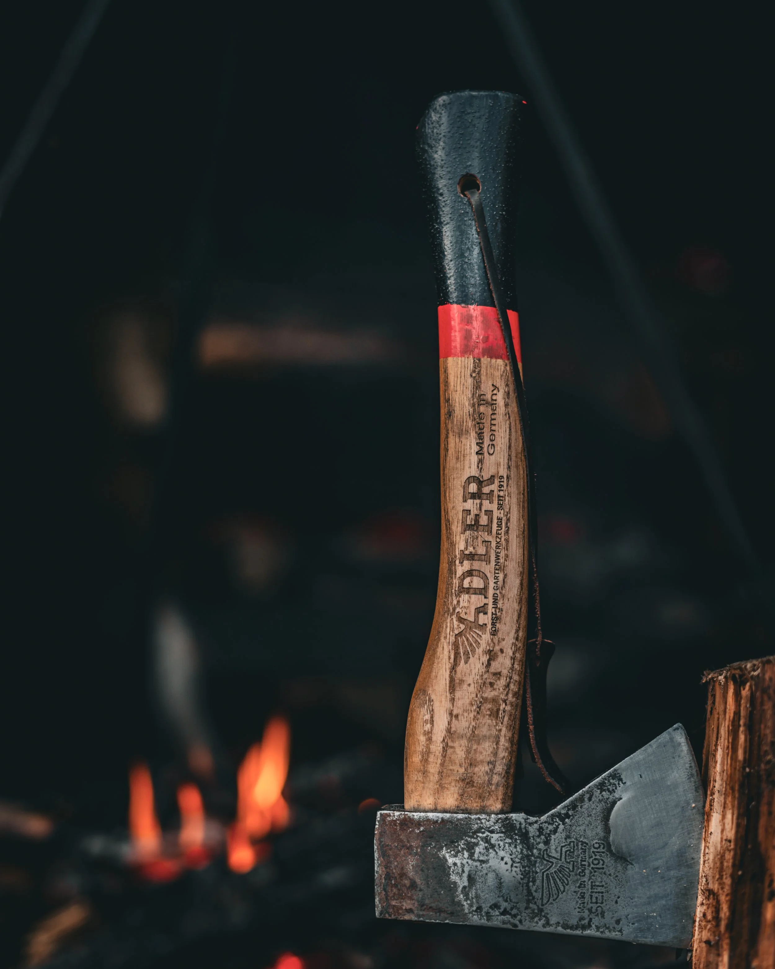 An axe with a wooden handle and metal head is embedded in a piece of wood, with small flames and sparks in the background.