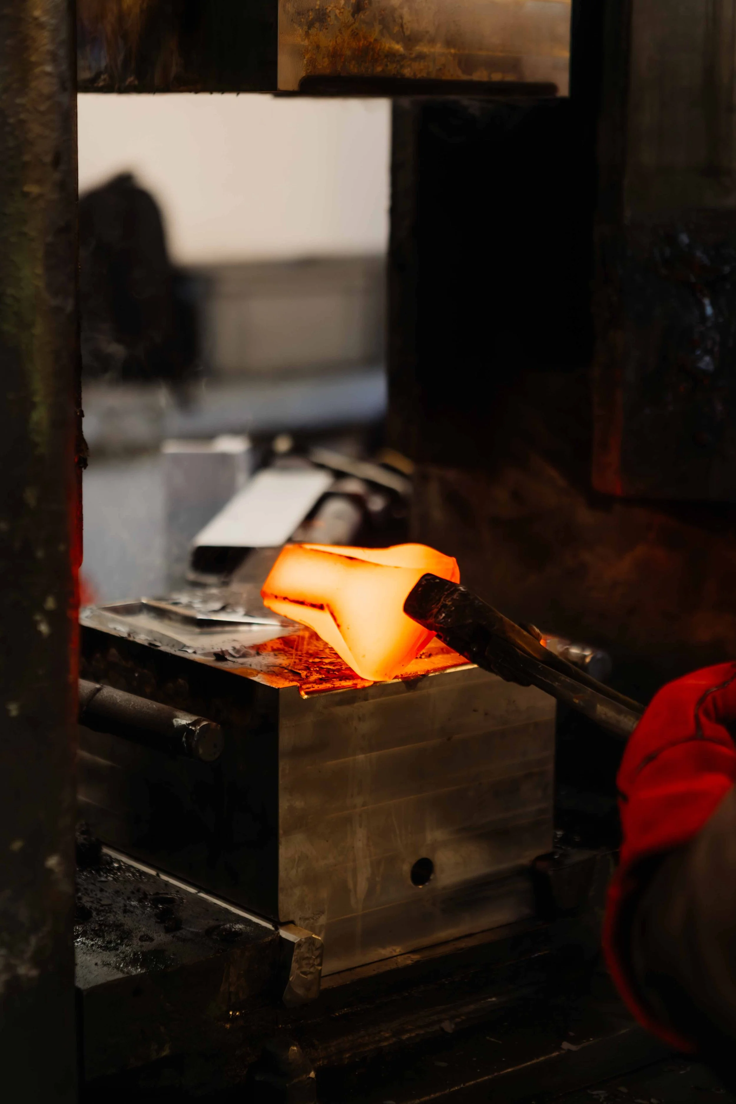 A glassblowing process showing molten glass being shaped with a metal tool in a workshop.