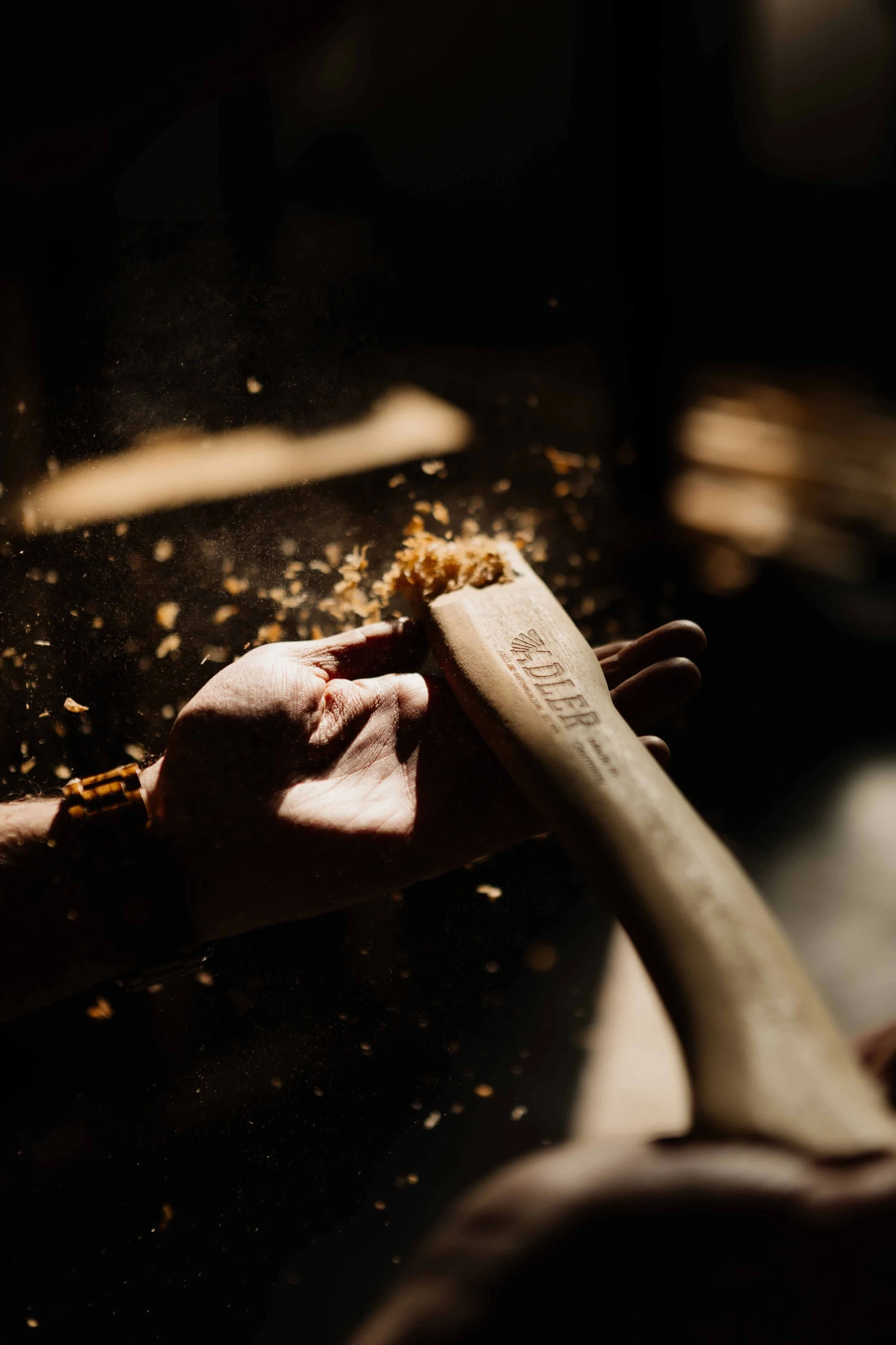 Close-up of a person’s hand using a wooden mallet to hammer a dough. Flour or dust is flying in the air, indicating active kneading or pounding.