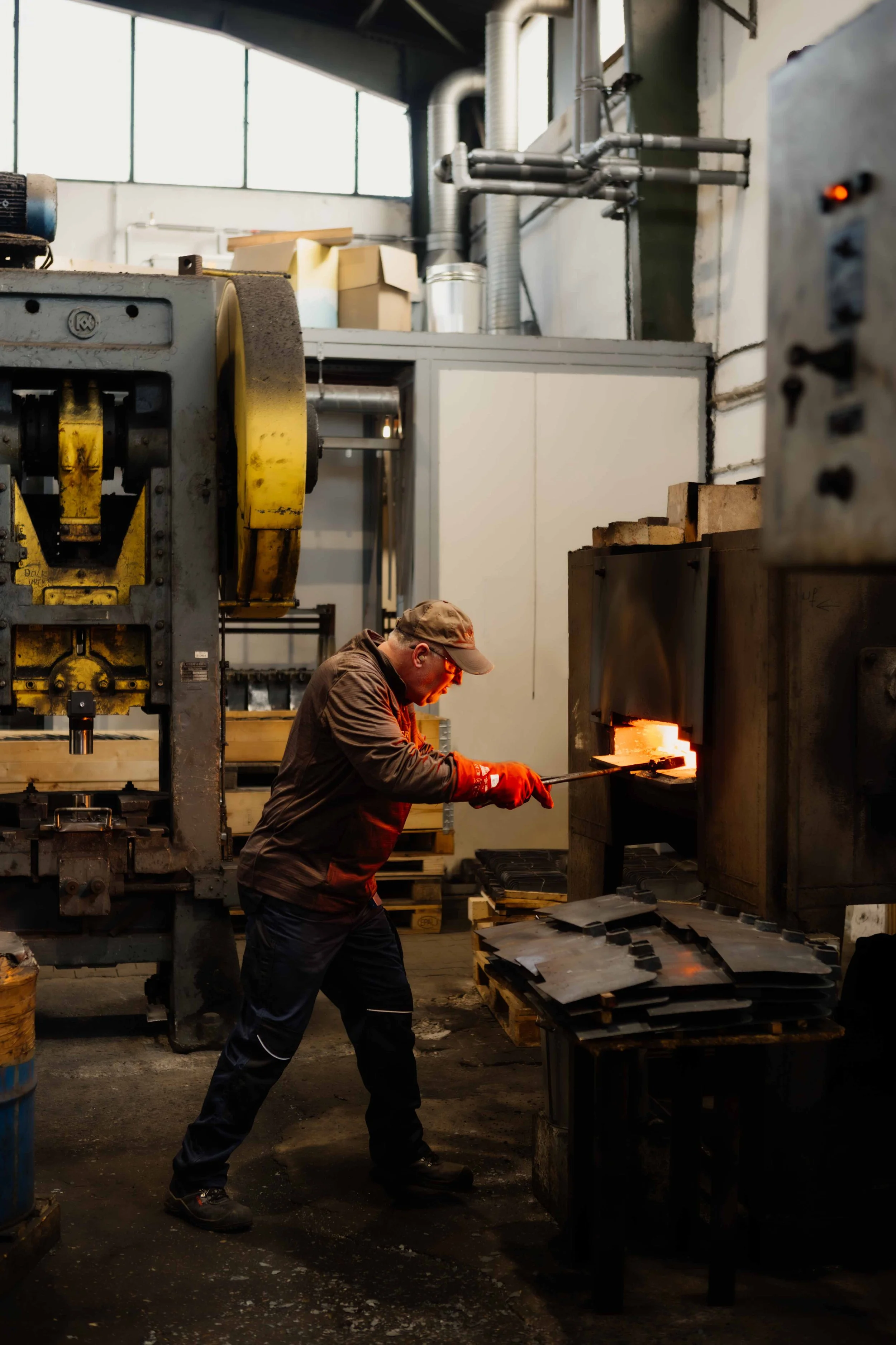 A worker in safety gear is melting metal in a forge inside an industrial workshop.