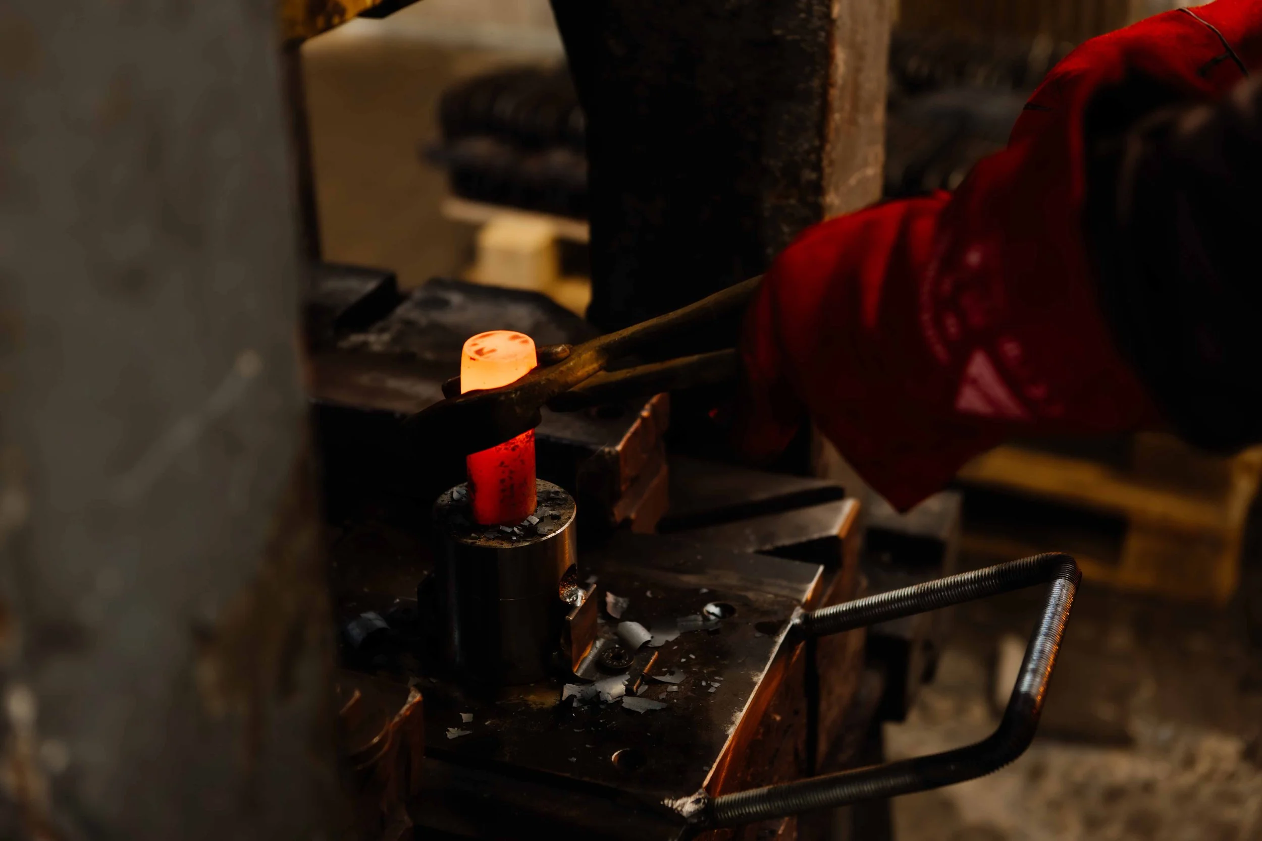 A blacksmith heating and shaping a piece of metal using a hammer on an anvil in a workshop.