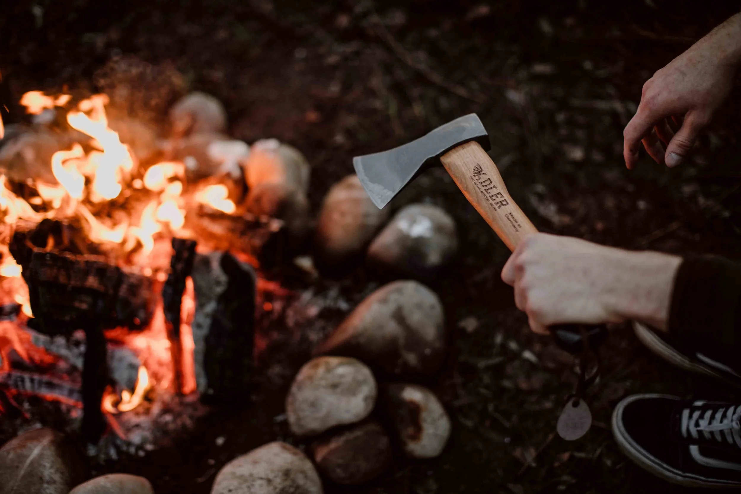 Person chopping wood with an axe near a campfire surrounded by rocks.