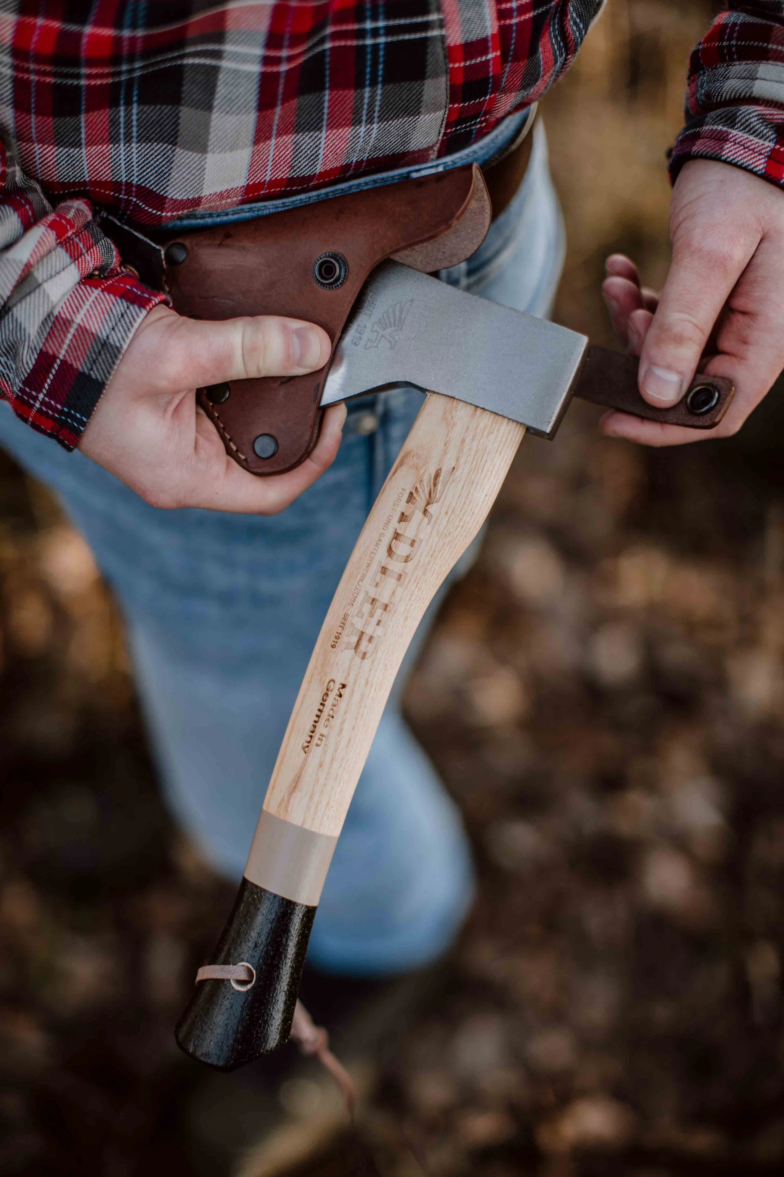Person wearing a red plaid shirt holding an axe with a wooden handle, preparing to chop wood outdoors.