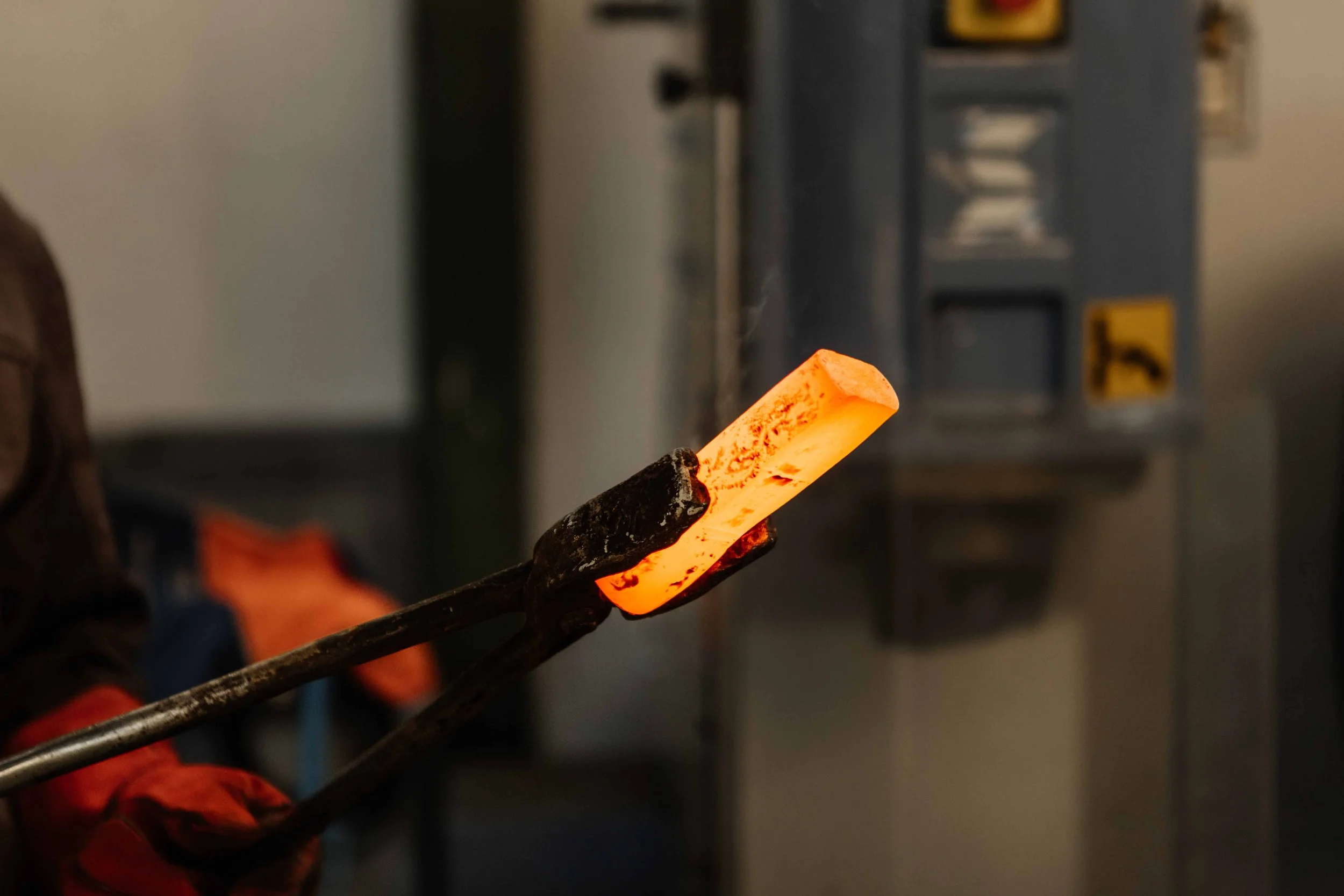 A glowing piece of hot metal being held with tongs in a metalworking shop.