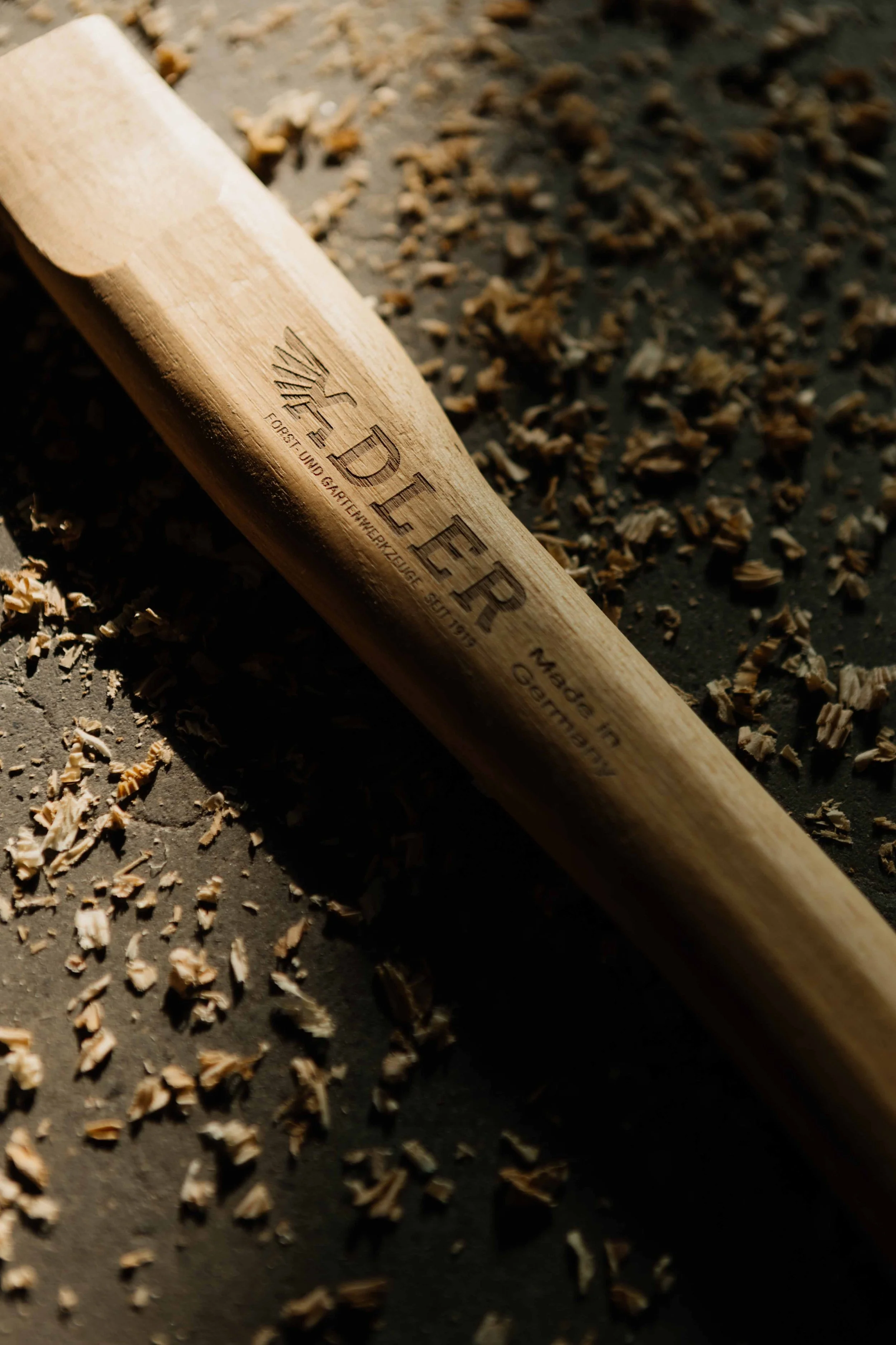 A wooden chisel tool on a dark surface with wood shavings scattered around.