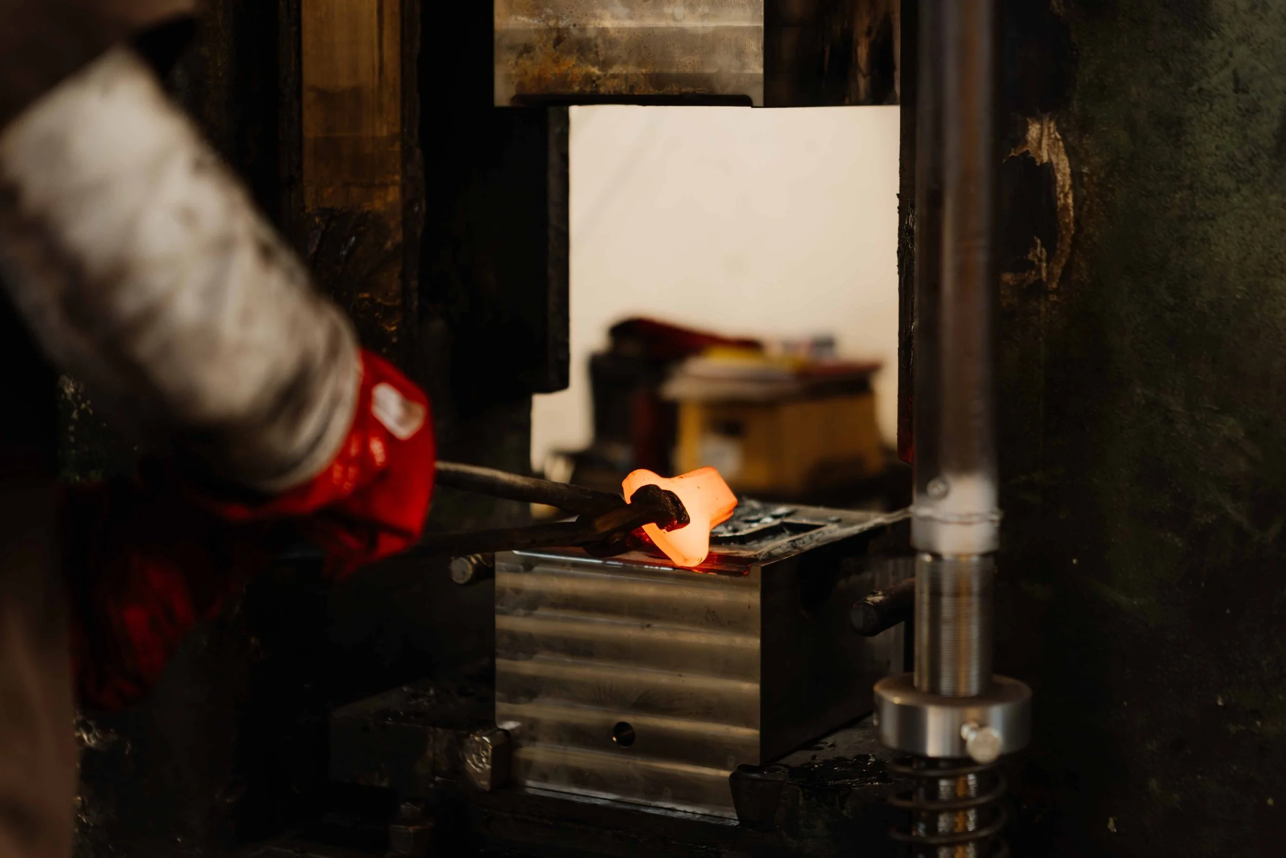A glassmaker using tongs to shape molten glass in a high-temperature furnace.