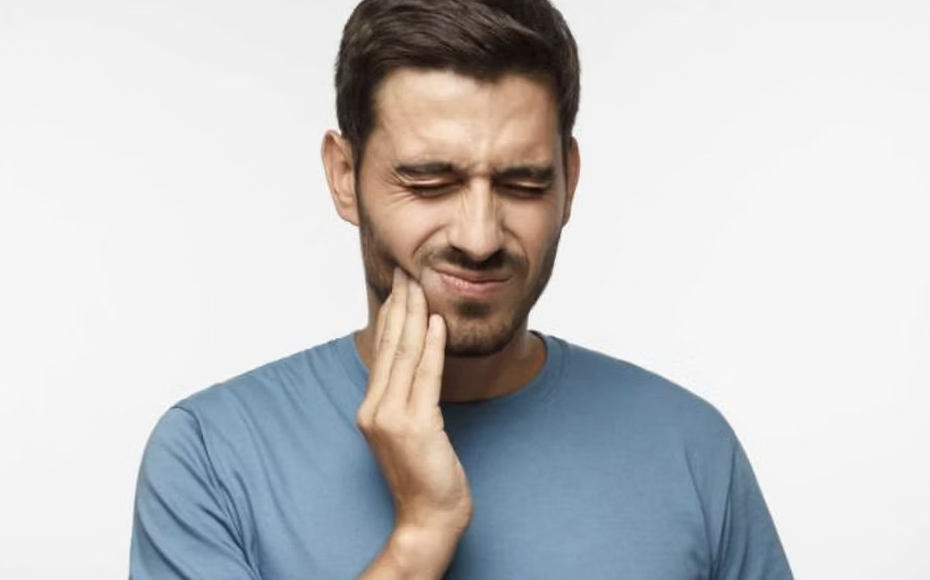 Man in a blue shirt holding his cheek, grimacing.