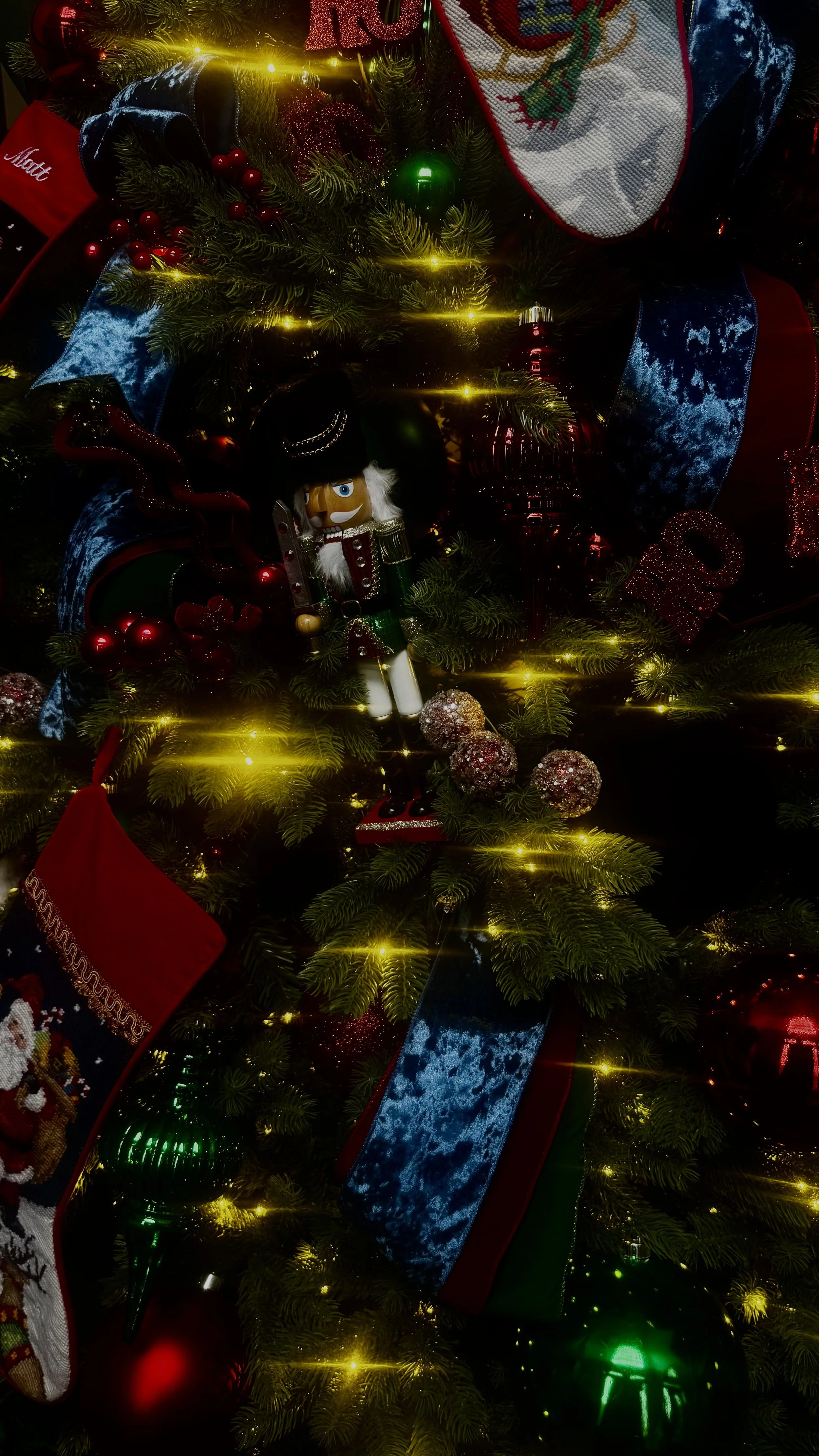 Close-up of a decorated Christmas tree with ornaments, ribbons, lights, and a Nutcracker figurine.