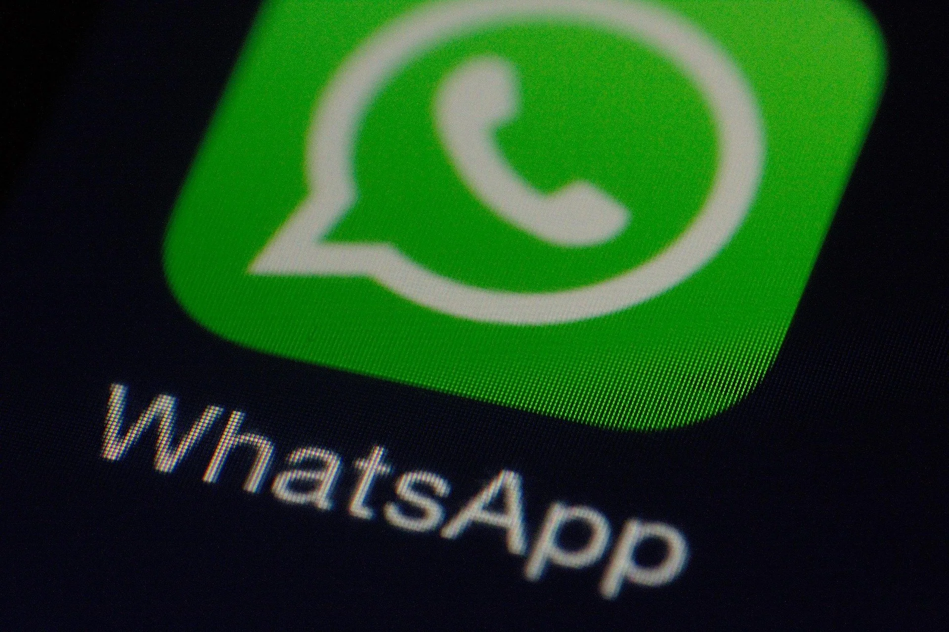 Close-up of a smartphone screen showing the WhatsApp app icon with green background and a white speech bubble with a phone inside. The text 'WhatsApp' appears below the icon.