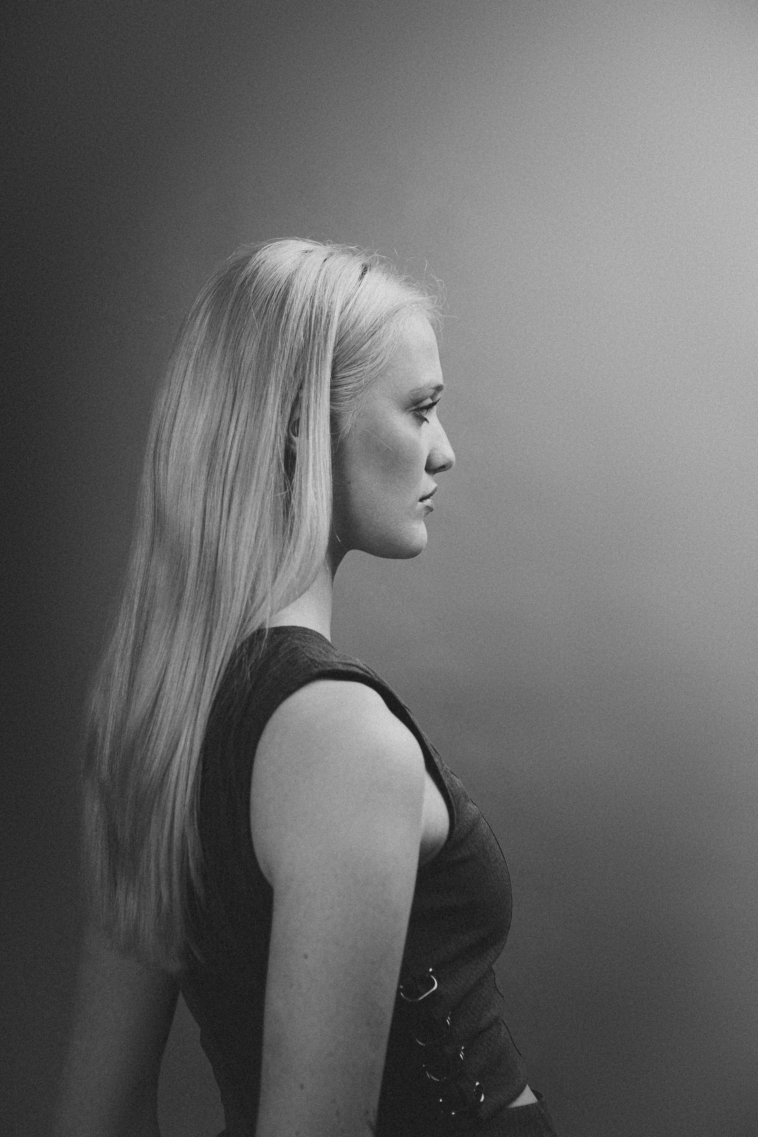 Black and white profile of a woman with long blonde hair wearing a sleeveless top, against a plain background.