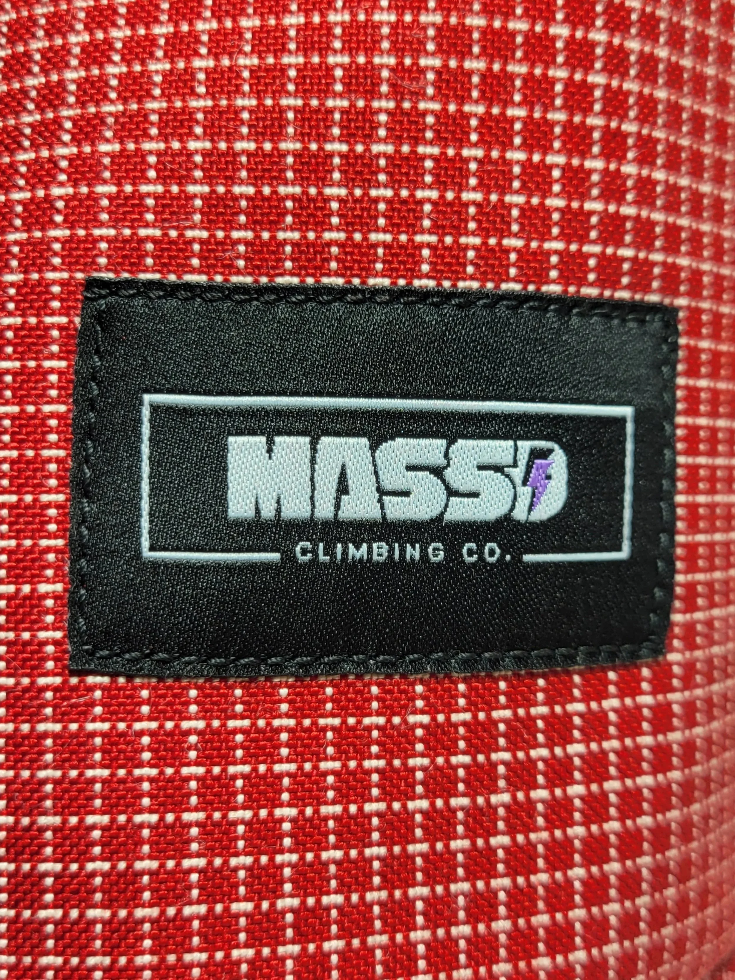 Close-up of a clothing label on red fabric, reading 'MASSD CLIMBING CO.' with a purple lightning bolt symbol.
