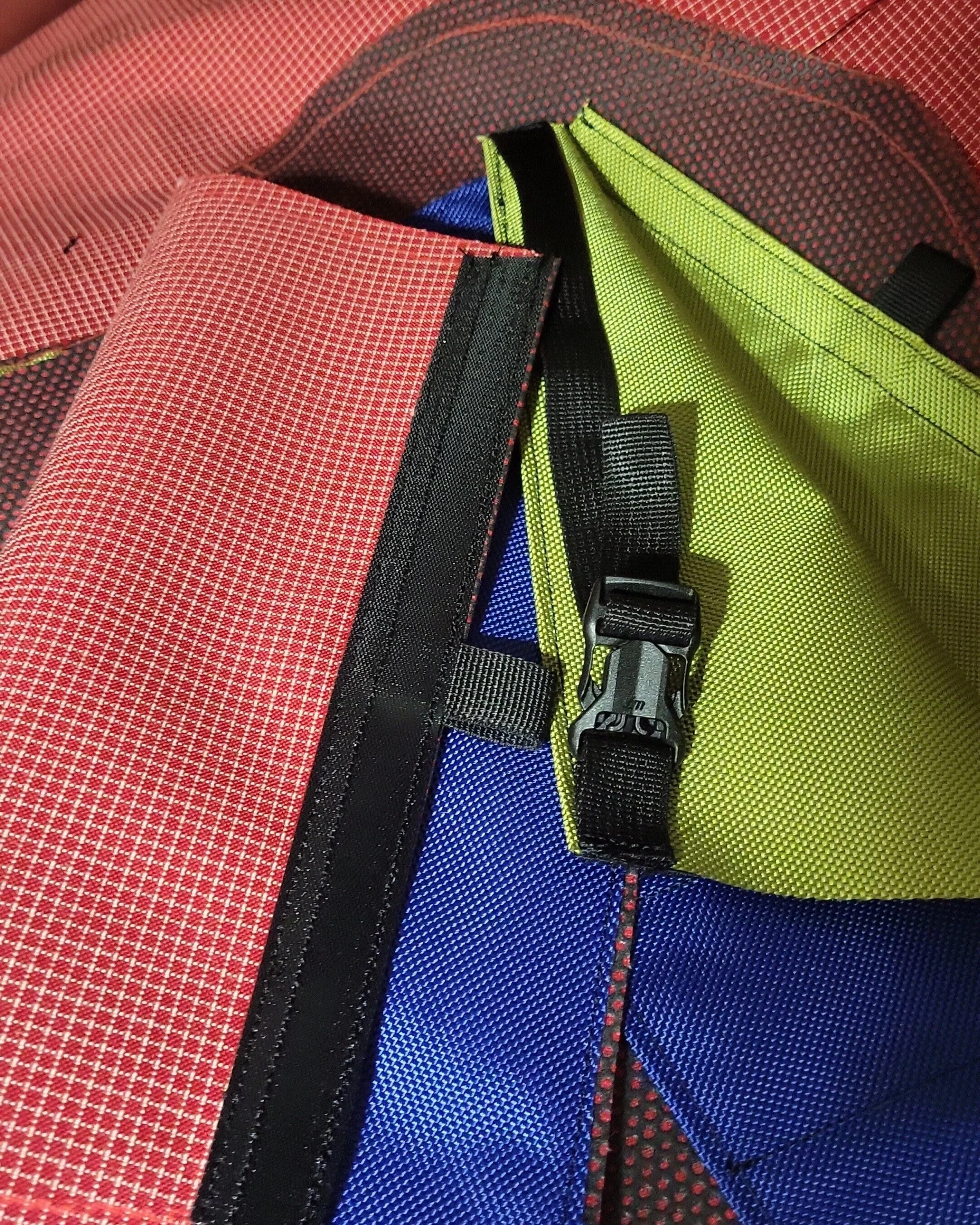 Close-up of a colorful bag with red, black, yellow, and blue fabric sections, featuring a black buckle and straps.