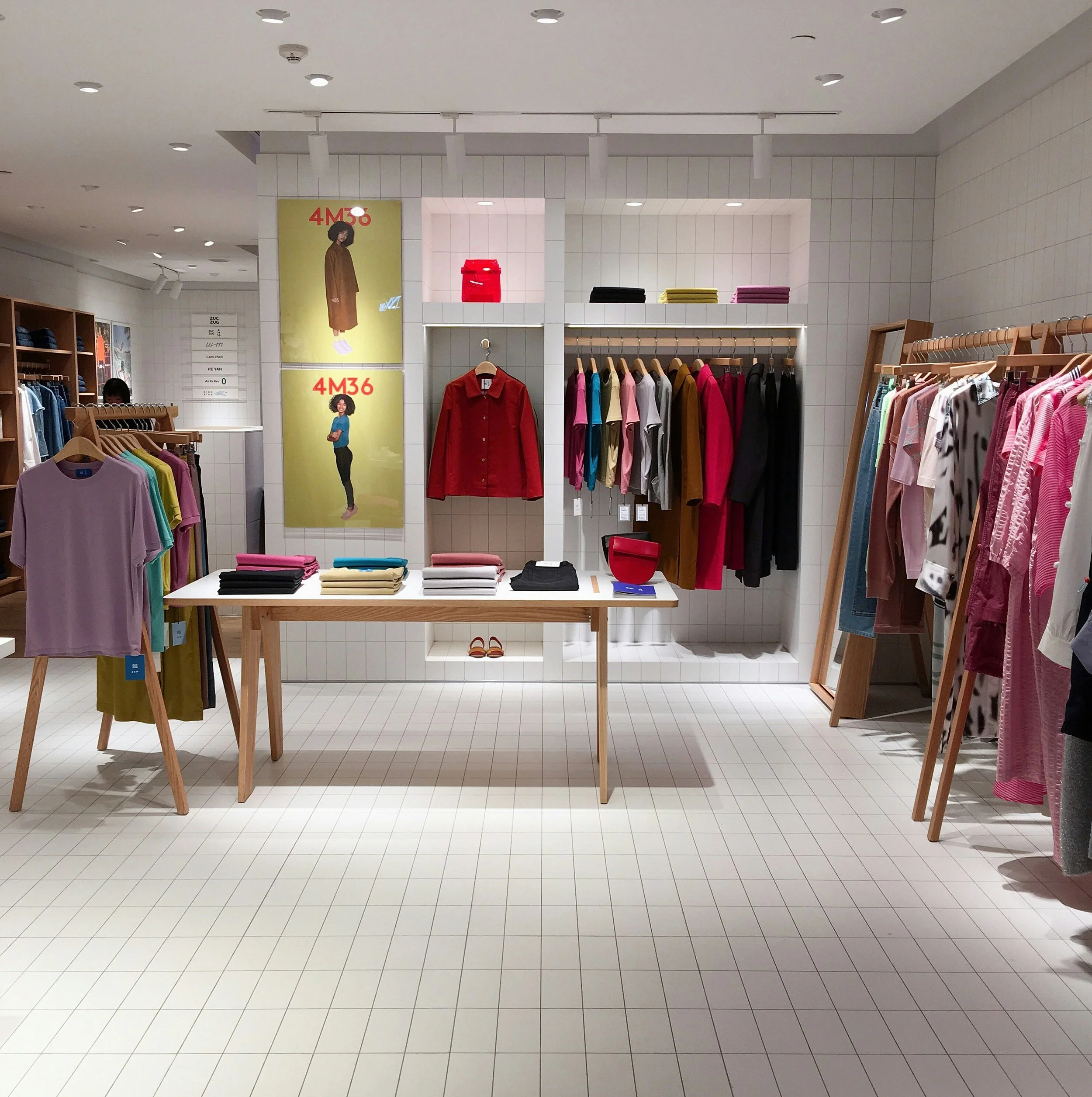 Clothing display in a store with racks of colorful clothes and a table with folded garments, shelves with accessories, and posters on the wall.