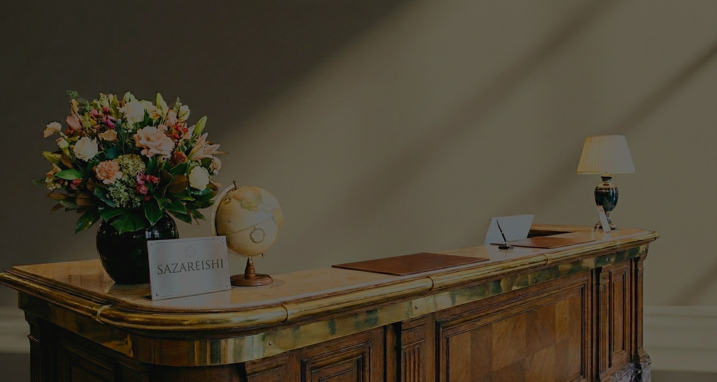 花の大きなアレンジメント、地球儀、受付のサイン、ランプがある木製のカウンター