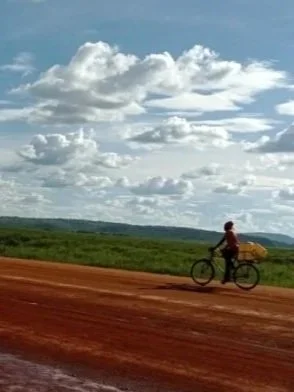 Person riding a bicycle on a dirt road under a cloudy sky.