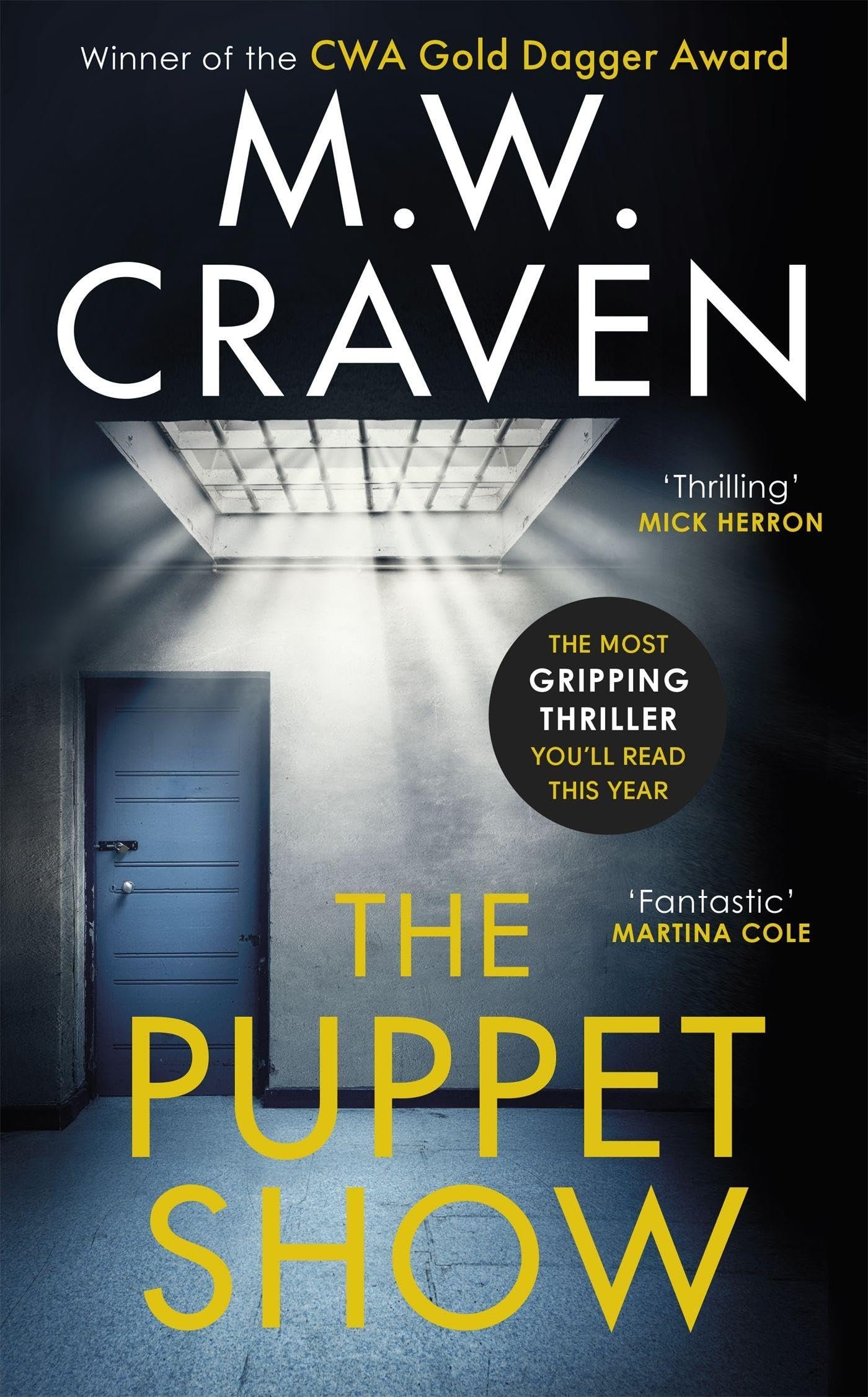 Book cover of The Puppet Show by M. W. Craven showing a blue door and barred ceiling in a dimly lit grey corridor.