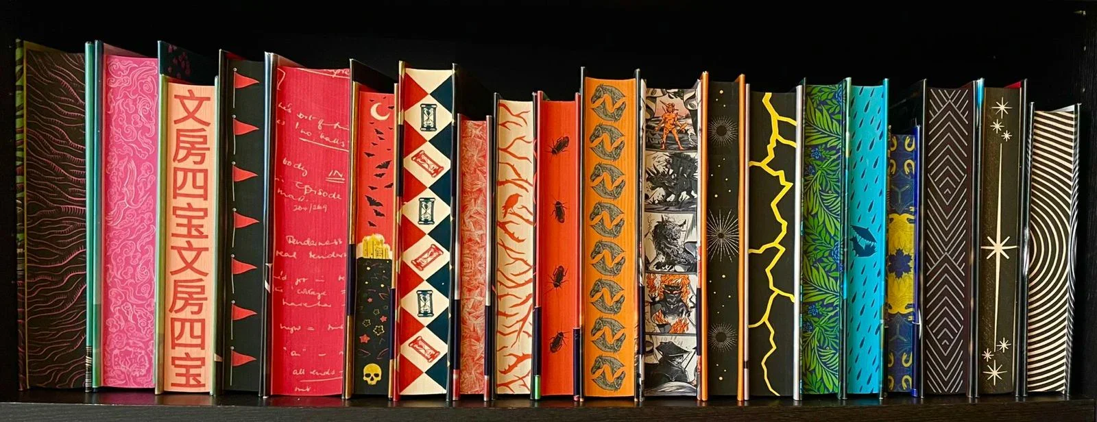 A row of colorful, patterned books standing upright on a shelf.