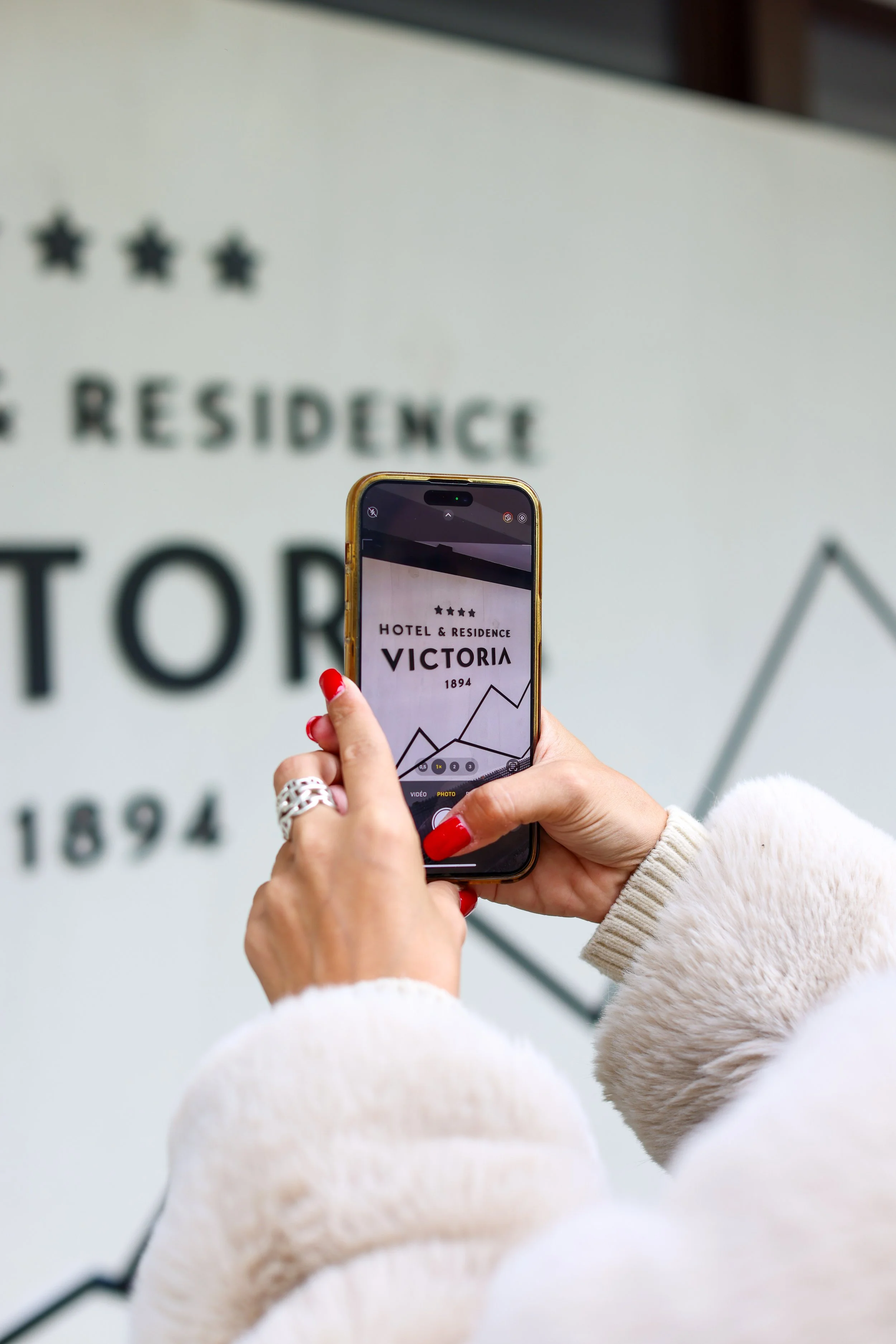 Une personne prenant une photo d'un panneau avec un téléphone, devant un panneau indiquant le nom d'un hôtel et résidence, Victoria, anciennement Hotel & Residence, construit en 1894.