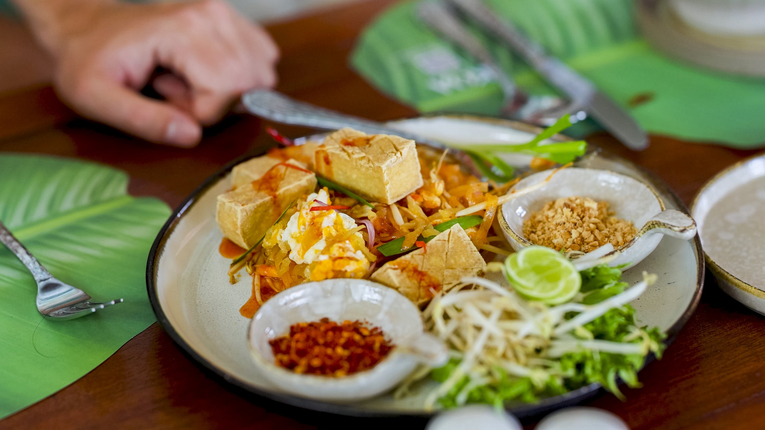 A plate of Mexican food featuring tofu, shredded vegetables, fresh greens, lime, and specific seasonings and condiments.