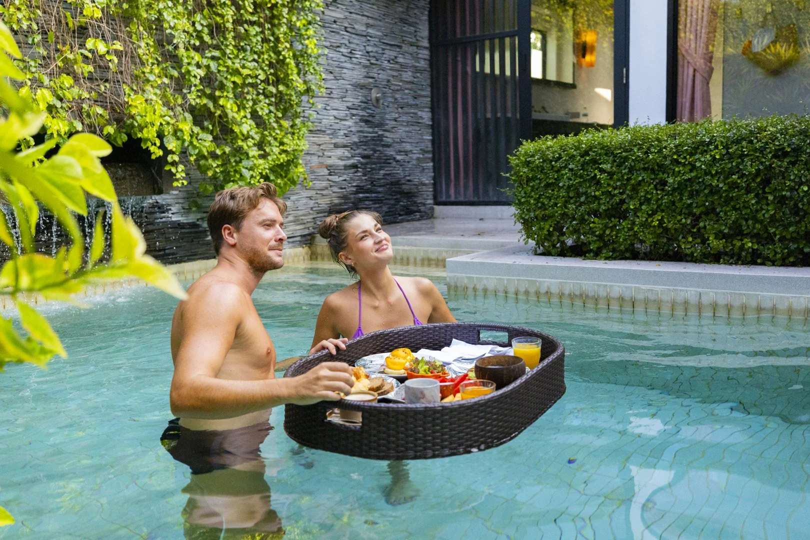 A man and woman in a swimming pool with a tray of breakfast food.