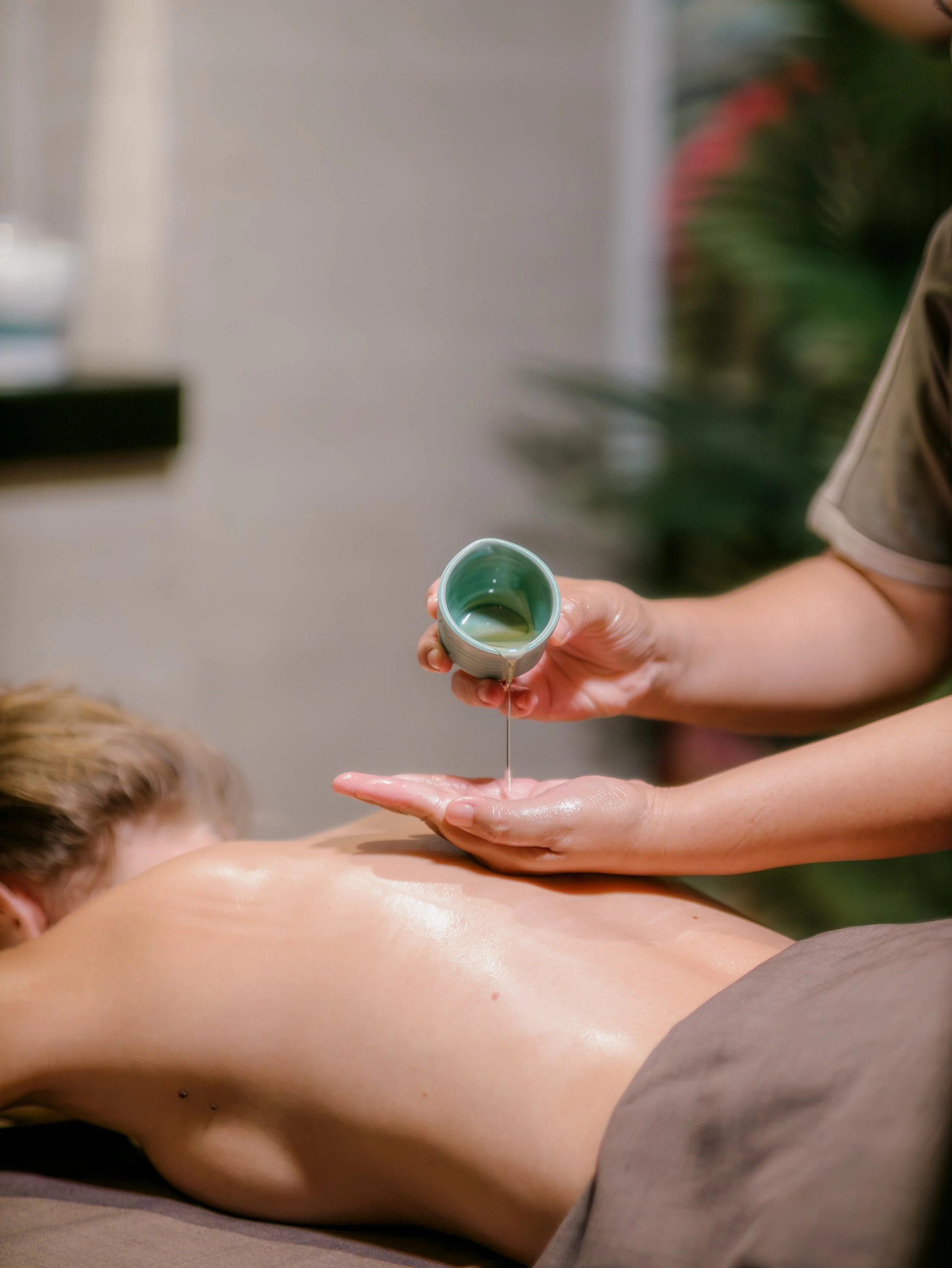 A person receiving a massage with massage oil being poured onto their back from a small bowl.