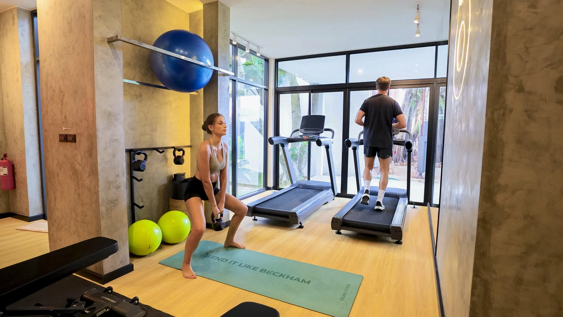 Man and woman exercising in a modern gym with windows and fitness equipment.
