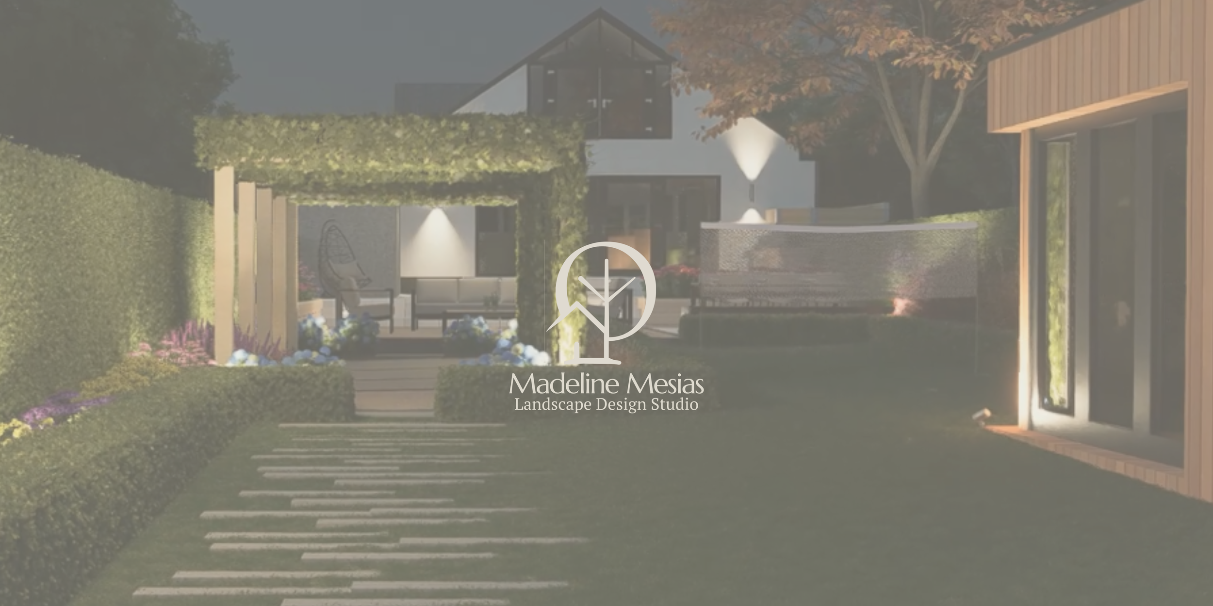 A landscaped backyard with a pathway, hedge, flowering plants, patio seating area, modern house with large windows, and a tree with autumn leaves.