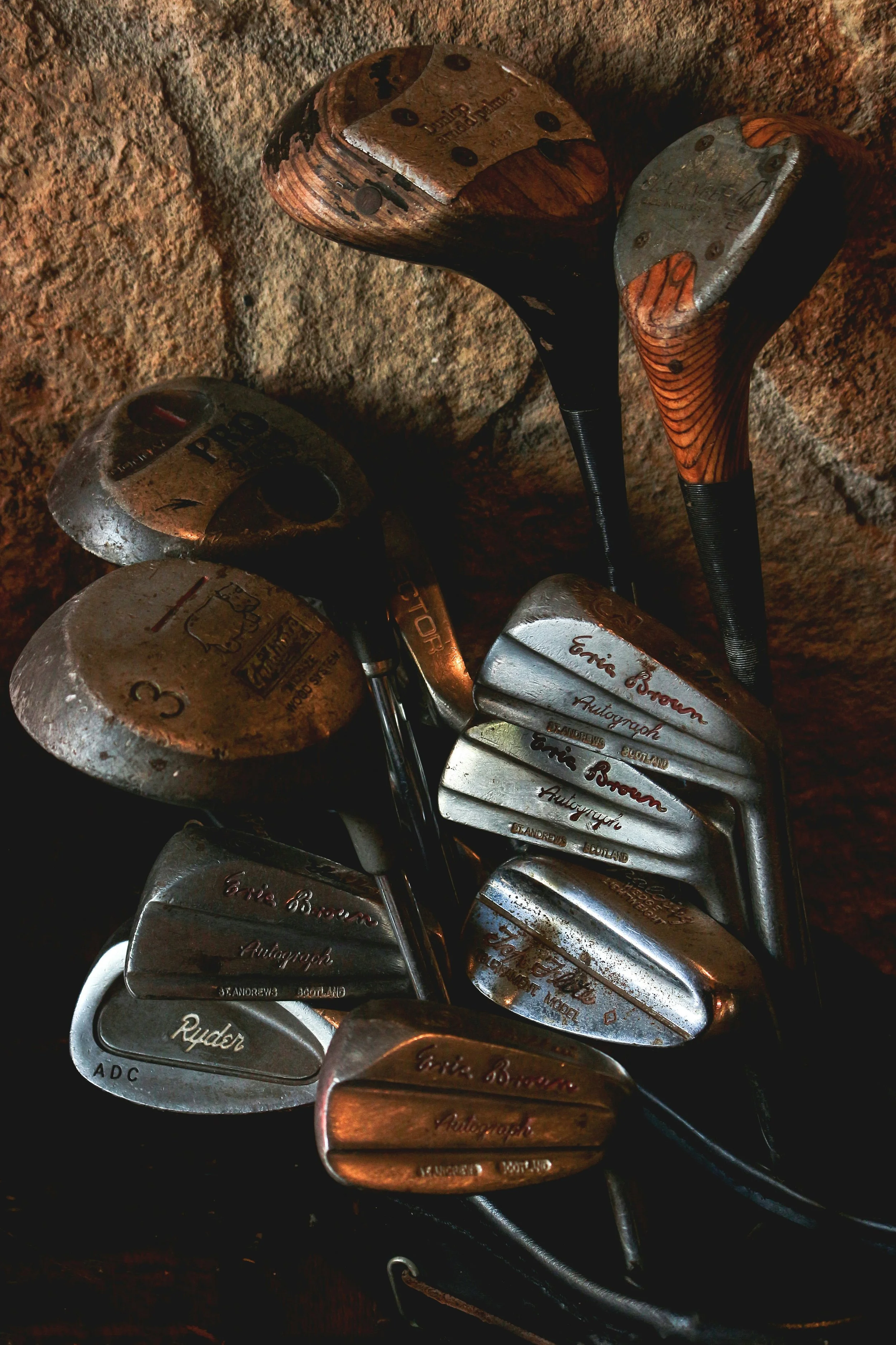 Collection of golf clubs leaning against a stone wall.