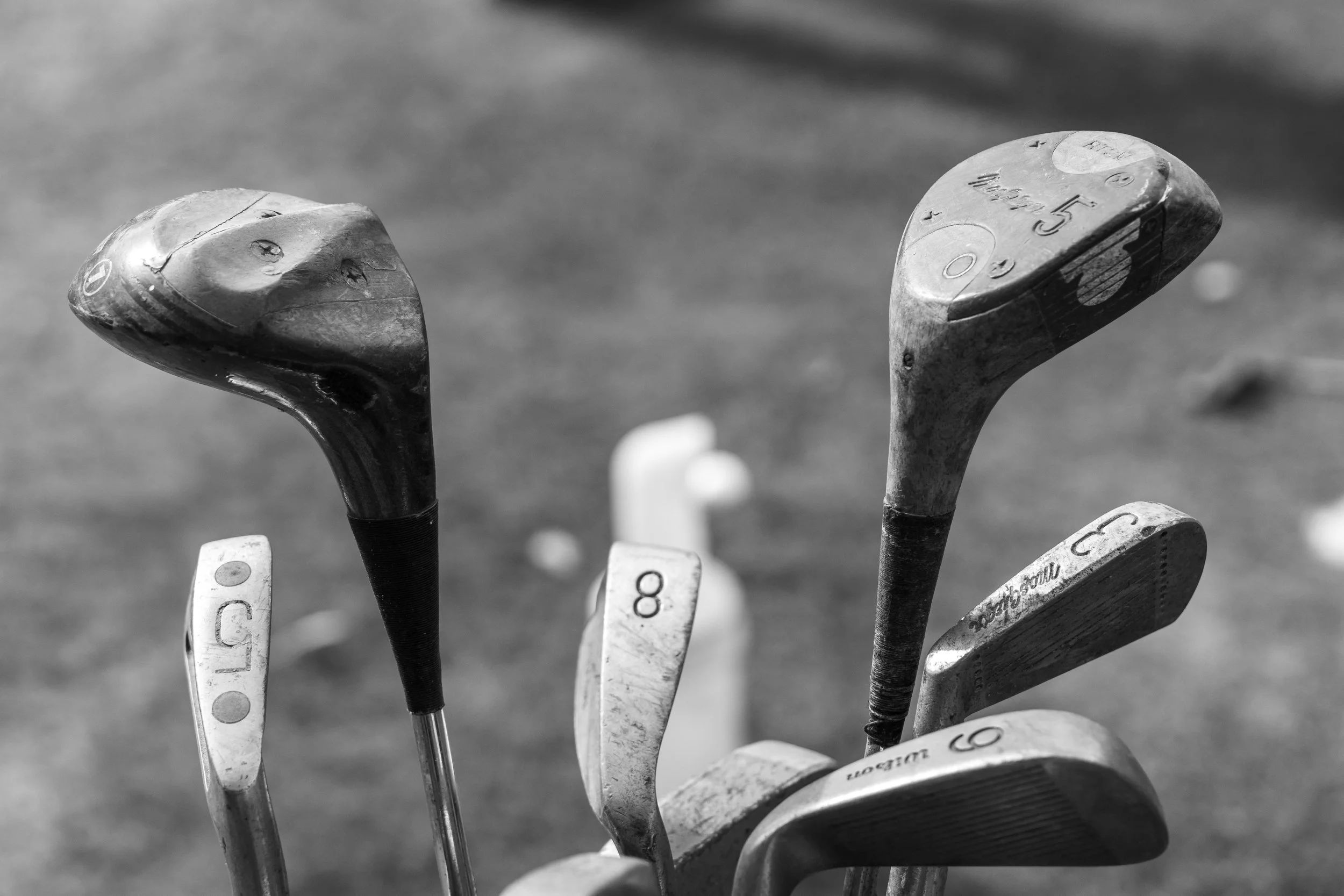 Close-up of golf clubs with worn heads and shafts, standing on a golf course.