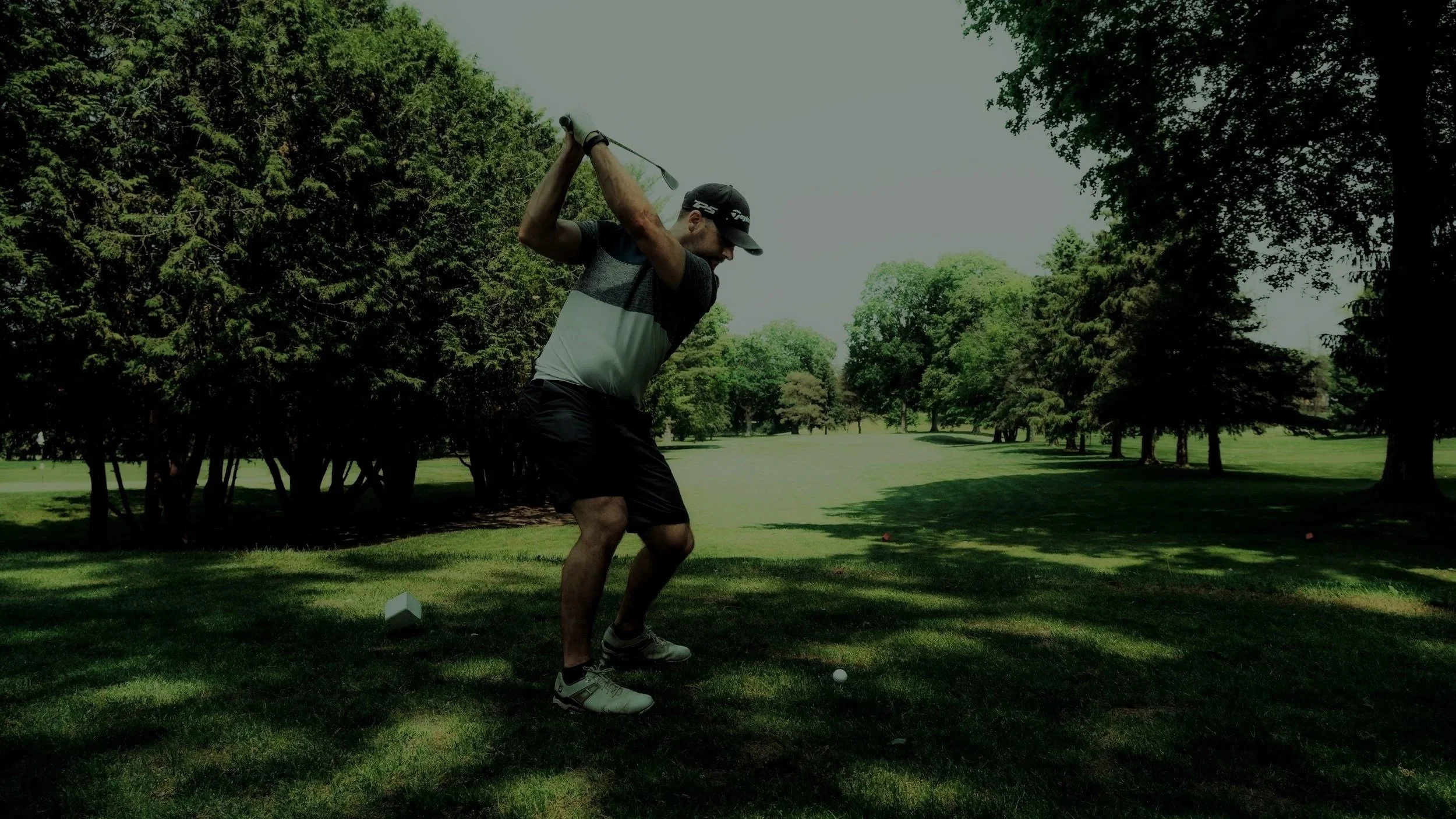 Man playing golf on a lush green golf course, preparing to hit a golf ball, surrounded by trees.