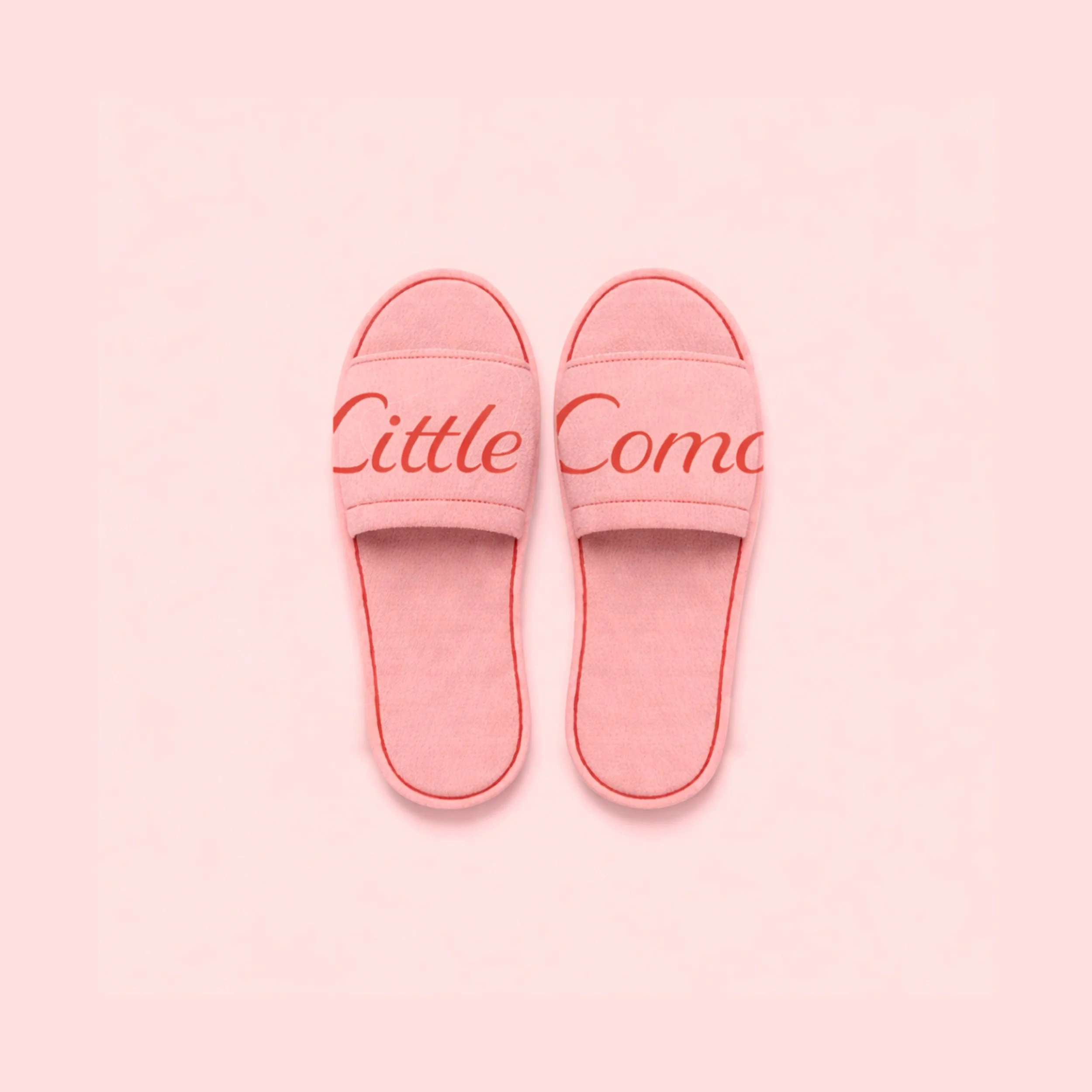 Pink slippers with the words "Little Come" written on the top strap, placed on a pink background.