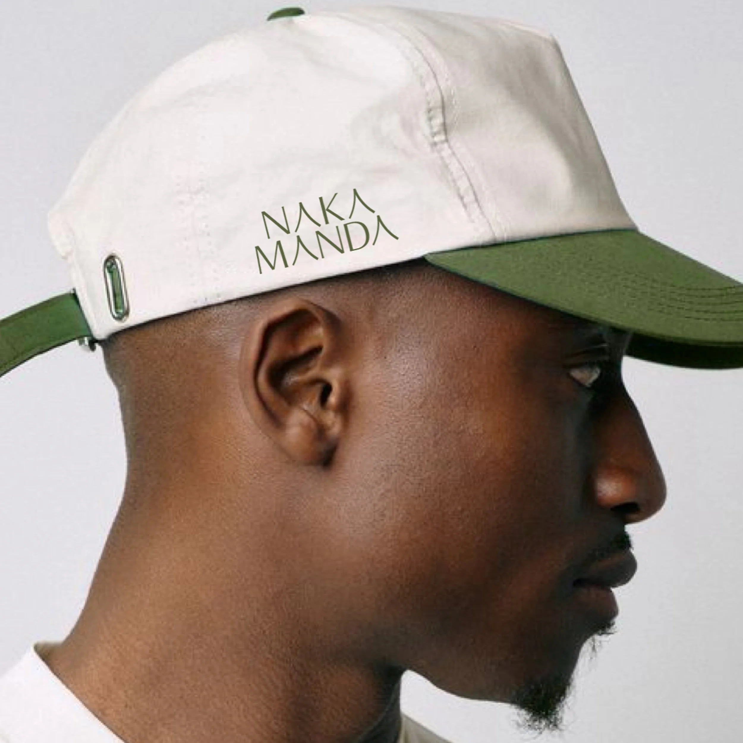 Side profile of a man wearing a white and green cap with the logo 'NAKA MANDA' on the front.