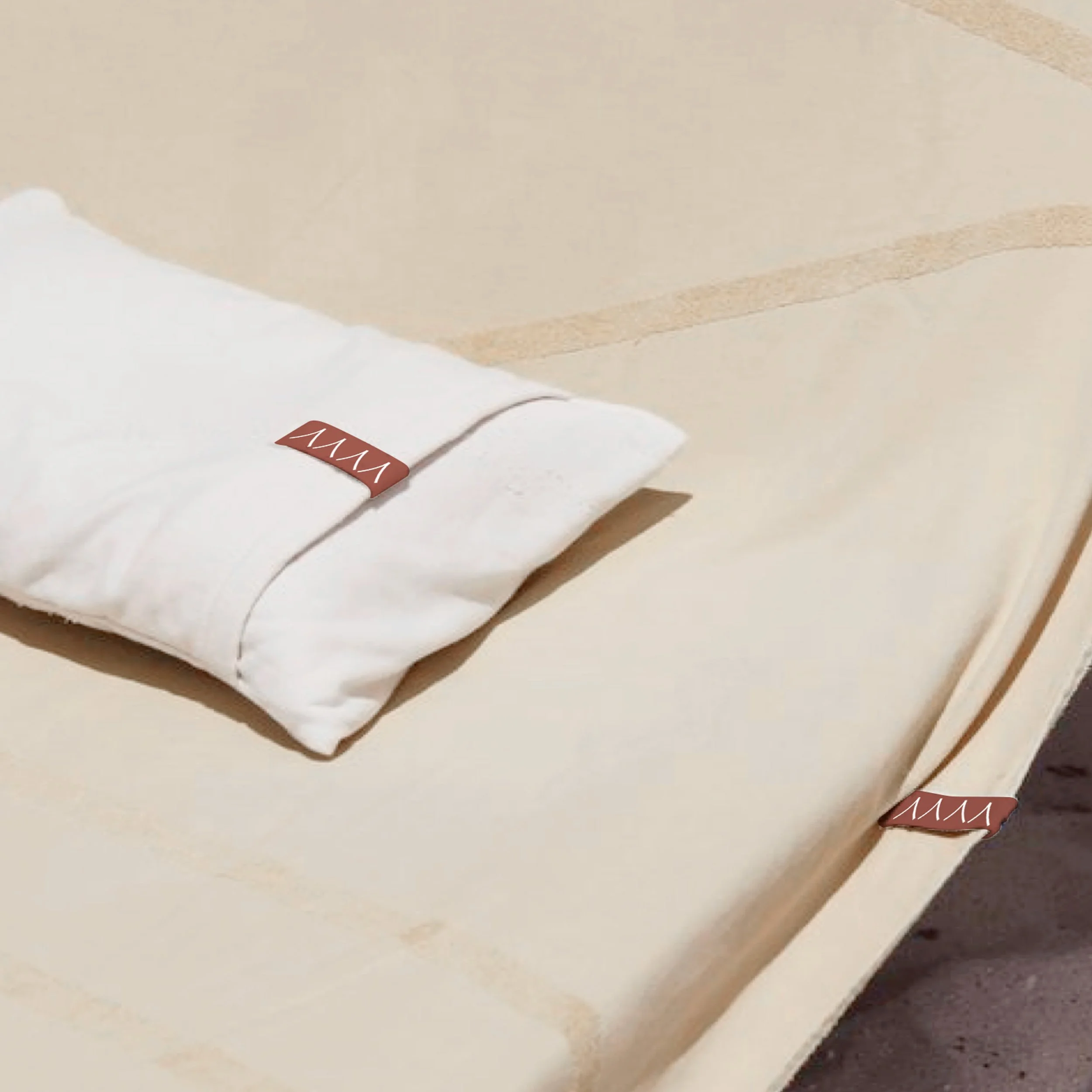 A neatly folded white bed sheet with a brown tag attached, resting on a light-colored bed or piece of furniture.