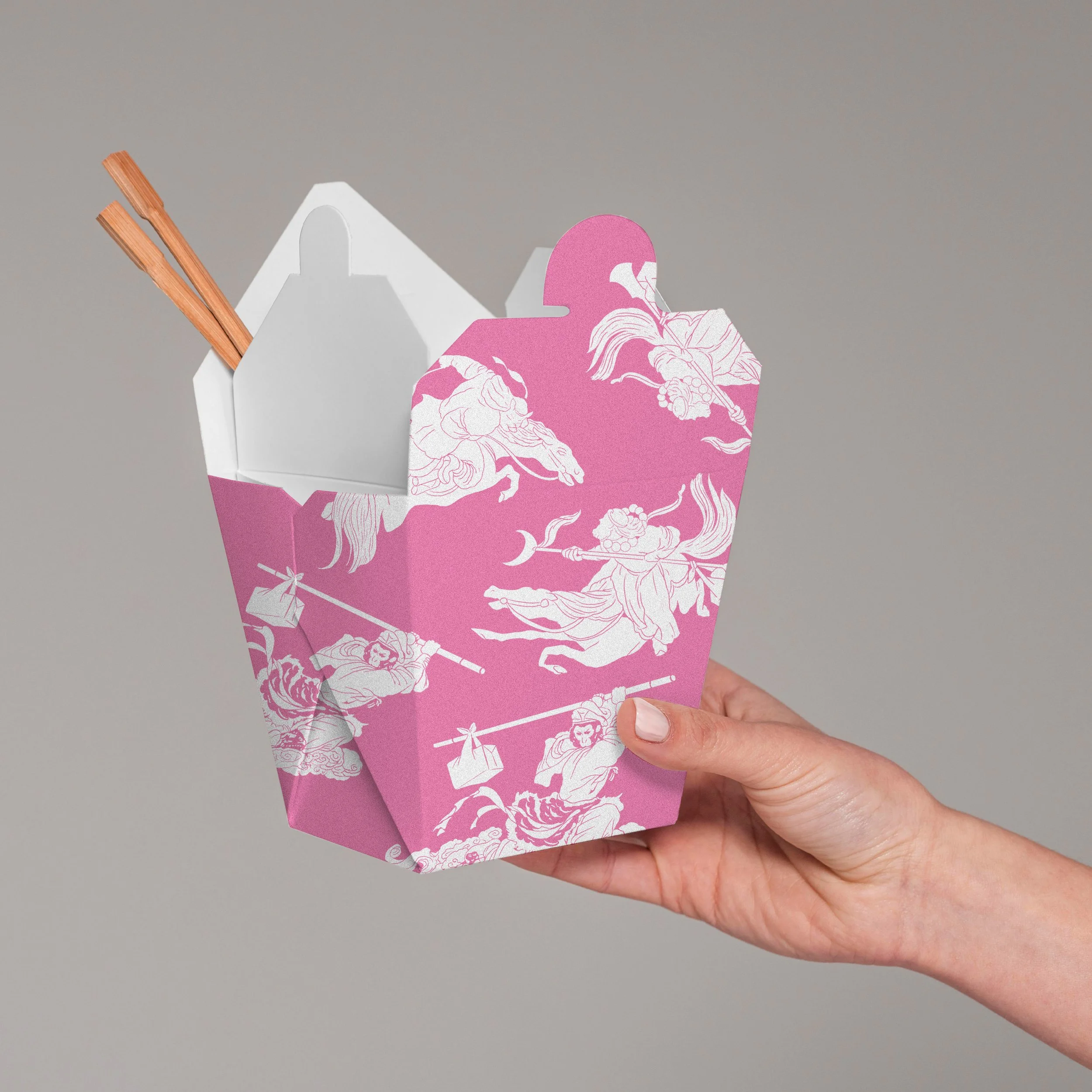 Hand holding a pink and white Asian-themed takeout box with chopsticks inside, featuring illustrations of warriors and mythical creatures.