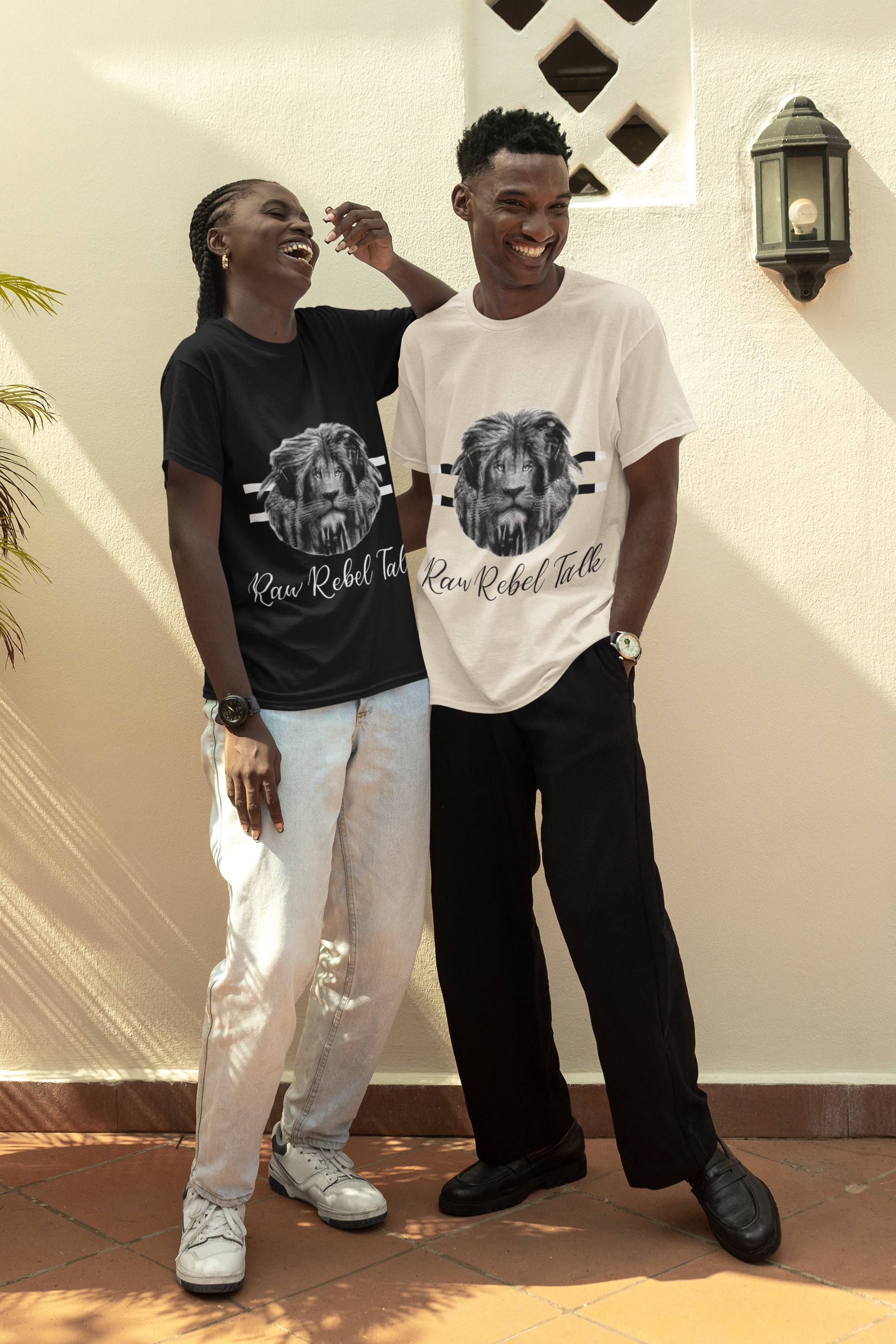 A woman and a man standing outdoors, both wearing matching T-shirts with a lion graphic and the text 'Raw Rebel Talk'. They are laughing and appear to be enjoying themselves.