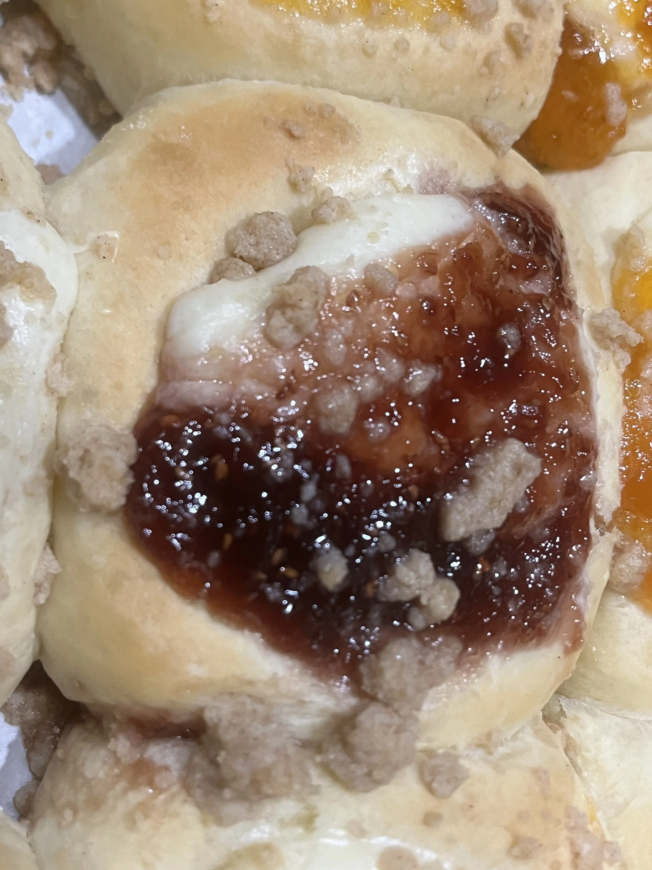 Close-up of a baked biscuit with fruit jam and crumb topping.